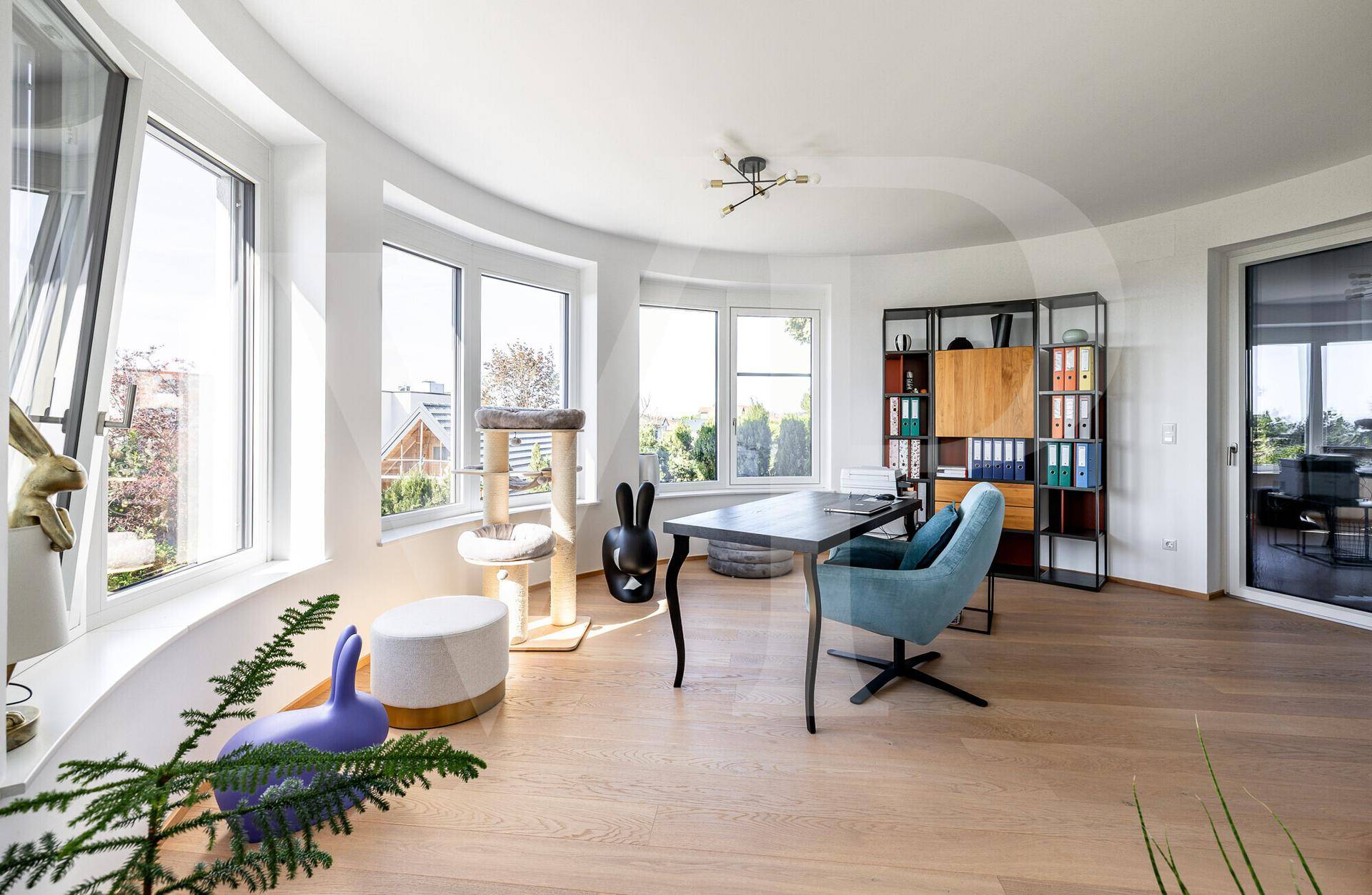 Helles Arbeitszimmer mit großen Fenstern, Holzboden und modernem Schreibtisch.