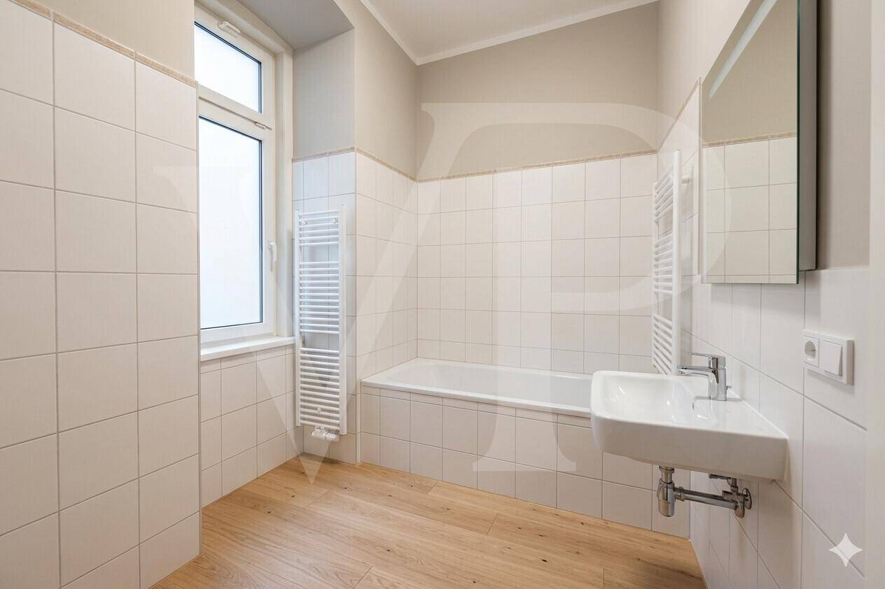 Modernes Badezimmer mit Badewanne, Waschbecken, beheiztem Handtuchhalter und Fenster für Tageslicht.