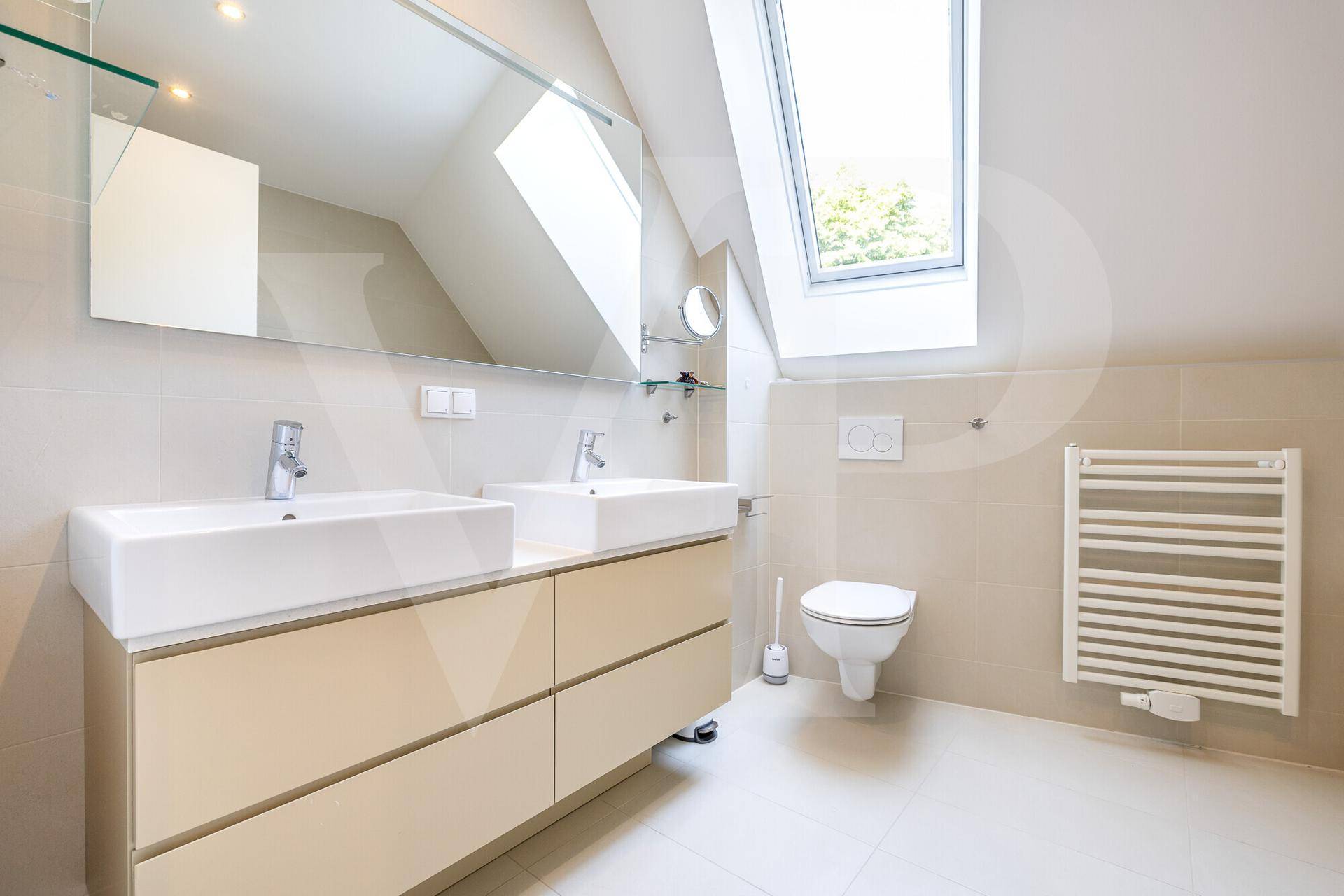 Modernes Badezimmer mit Doppelwaschbecken, Wand-WC, beheiztem Handtuchhalter und Dachfenster.