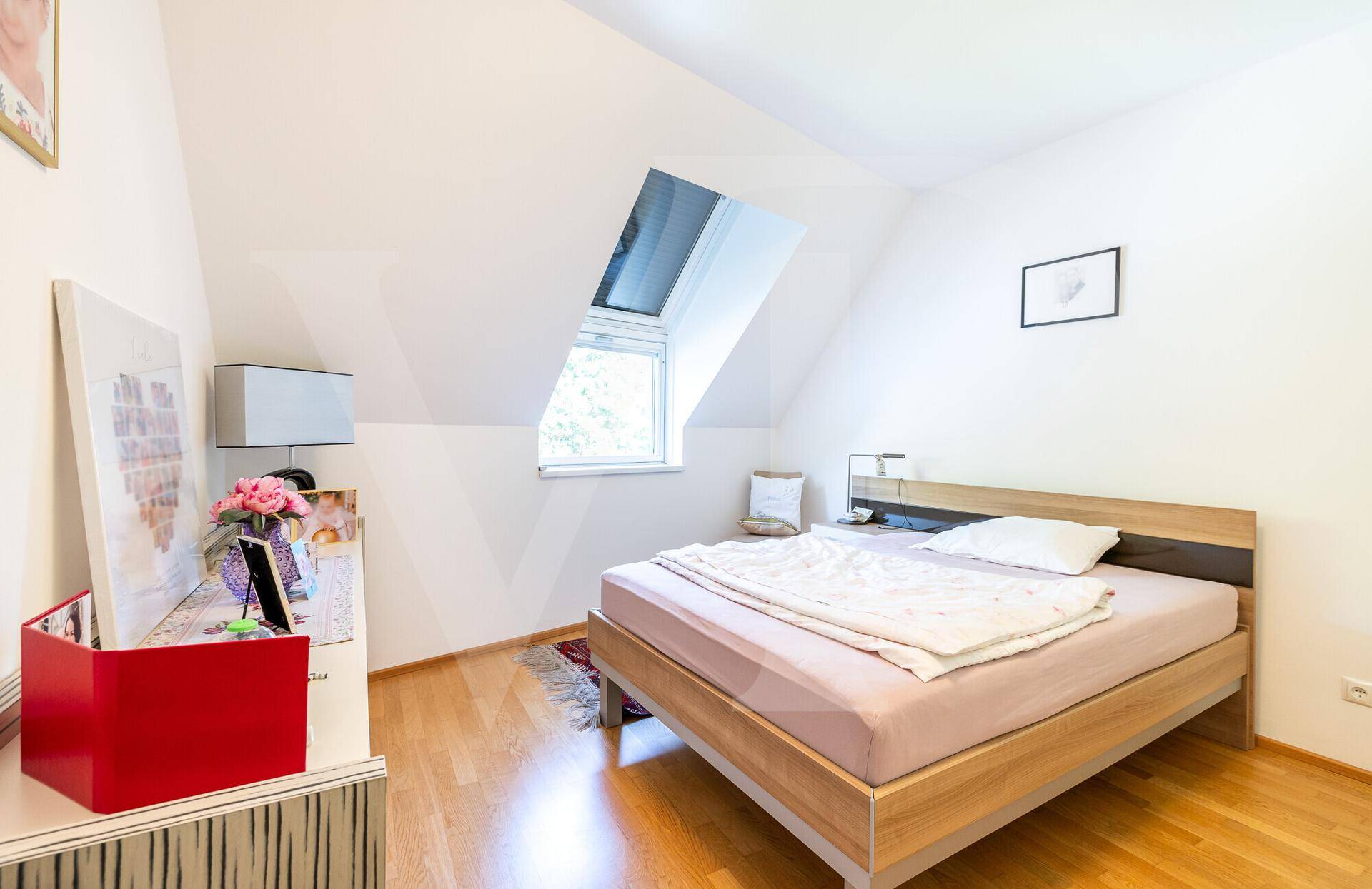 Helles Schlafzimmer im Dachgeschoss mit Holzboden, Doppelbett und Dachfenster für Tageslicht.