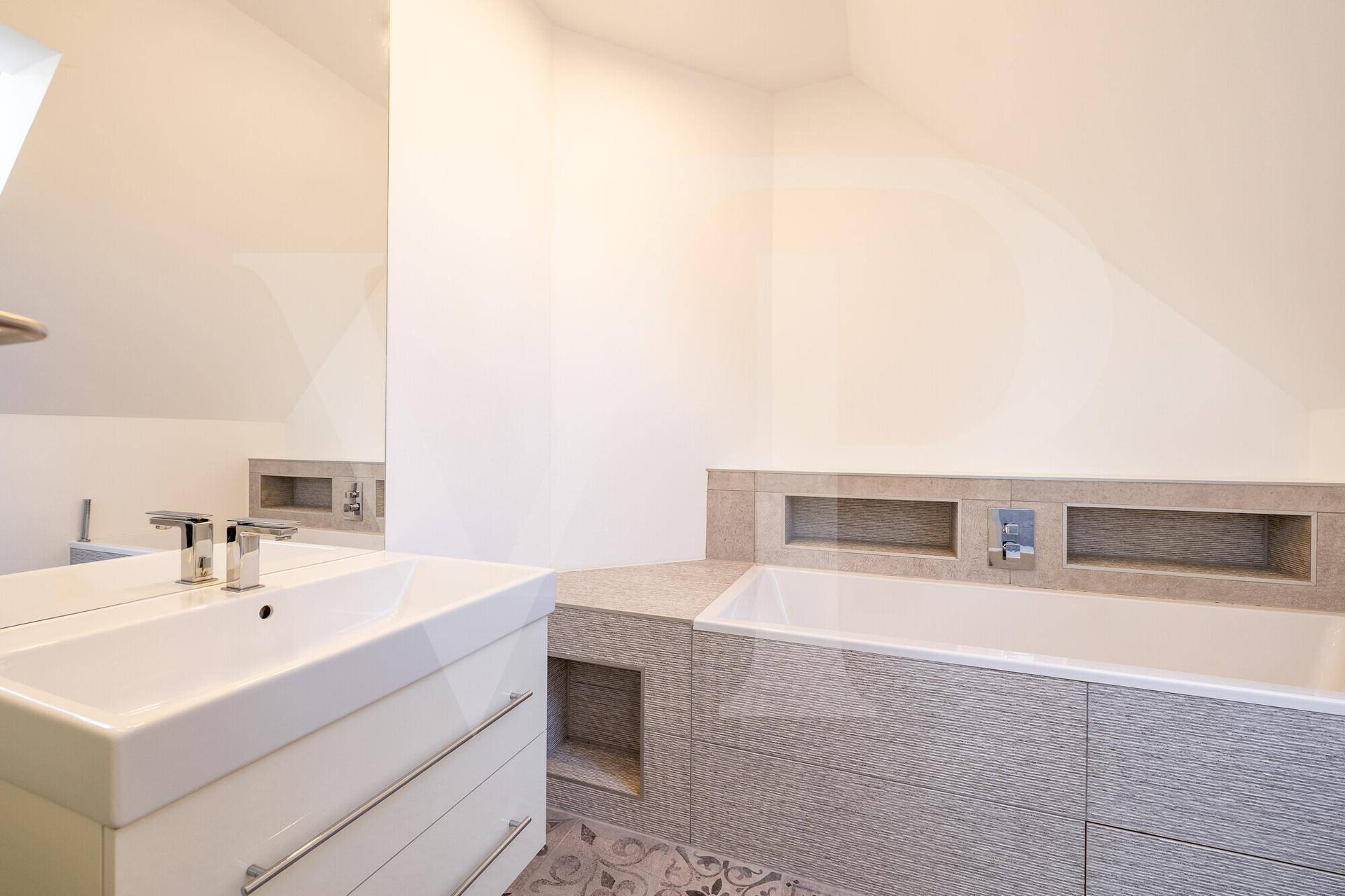 Modernes Badezimmer im Dachgeschoss mit Badewanne, Waschbecken und Dachschräge.