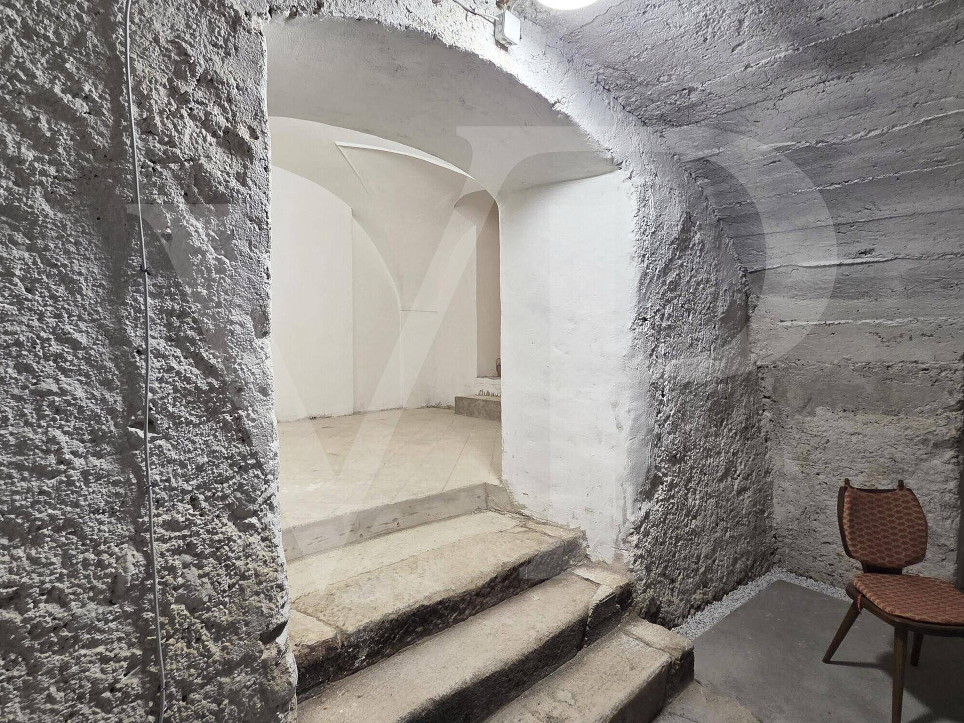 Treppenabgang in einen Gewölbekeller mit rauen Steinwänden und einfacher Beleuchtung.