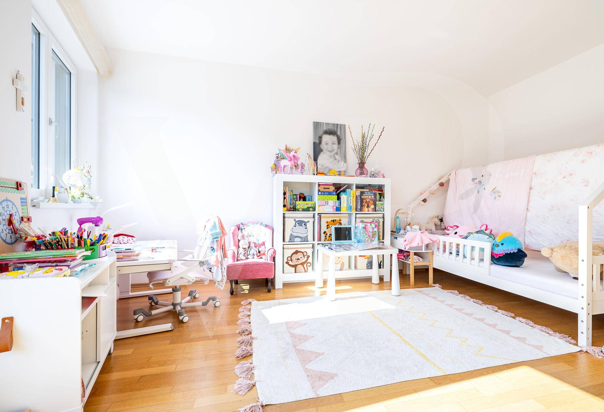 Kinderzimmer mit Holzboden, Spielzeug und einem kleinen Bett, hell und freundlich eingerichtet.