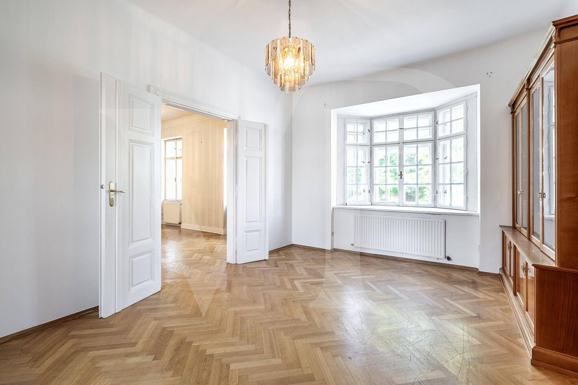Helles Zimmer mit Fischgrätparkett, einem Erkerfenster und einem eleganten Kronleuchter.