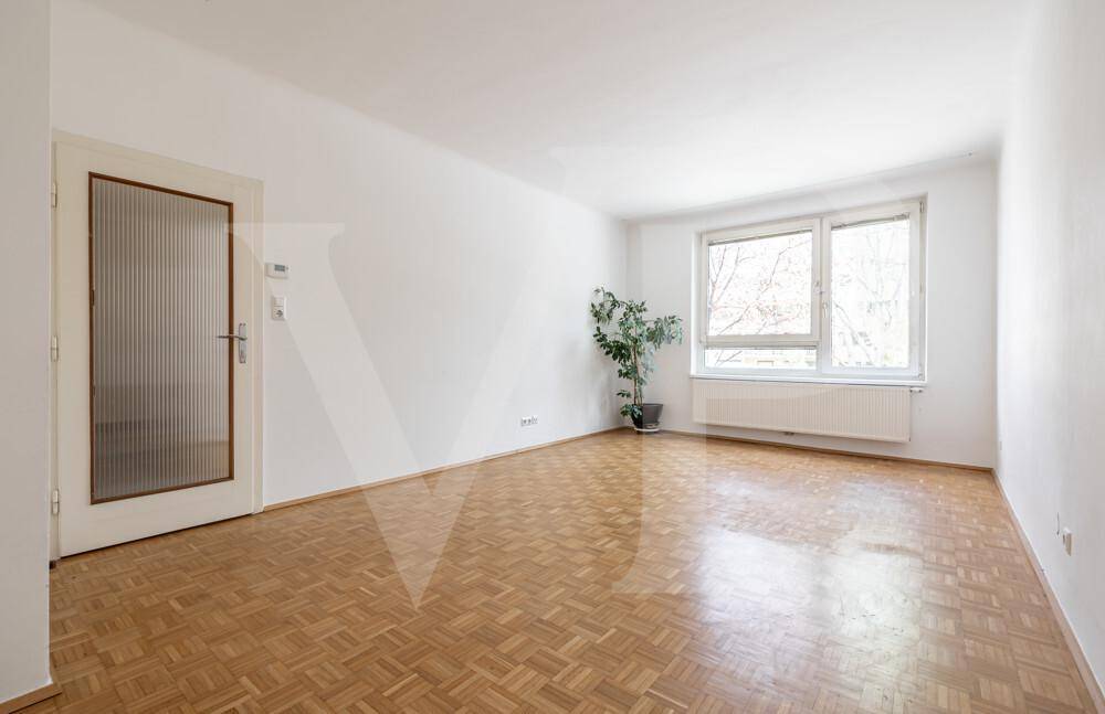 Helles Zimmer mit Parkettboden, großem Fenster und Zugangstür.