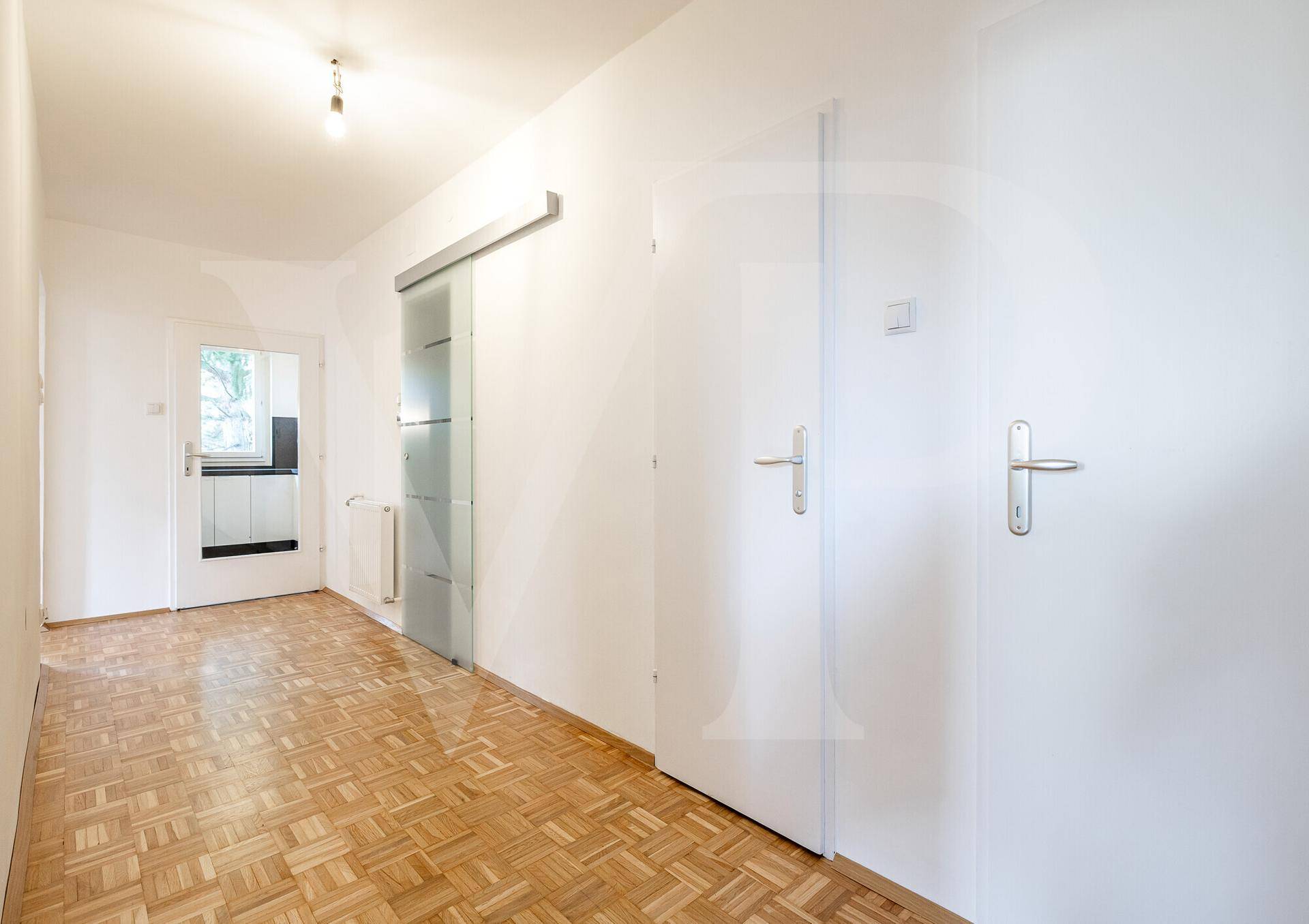 Geräumiger Flur mit Parkettboden, weißen Wänden und einer modernen Glasschiebetür.