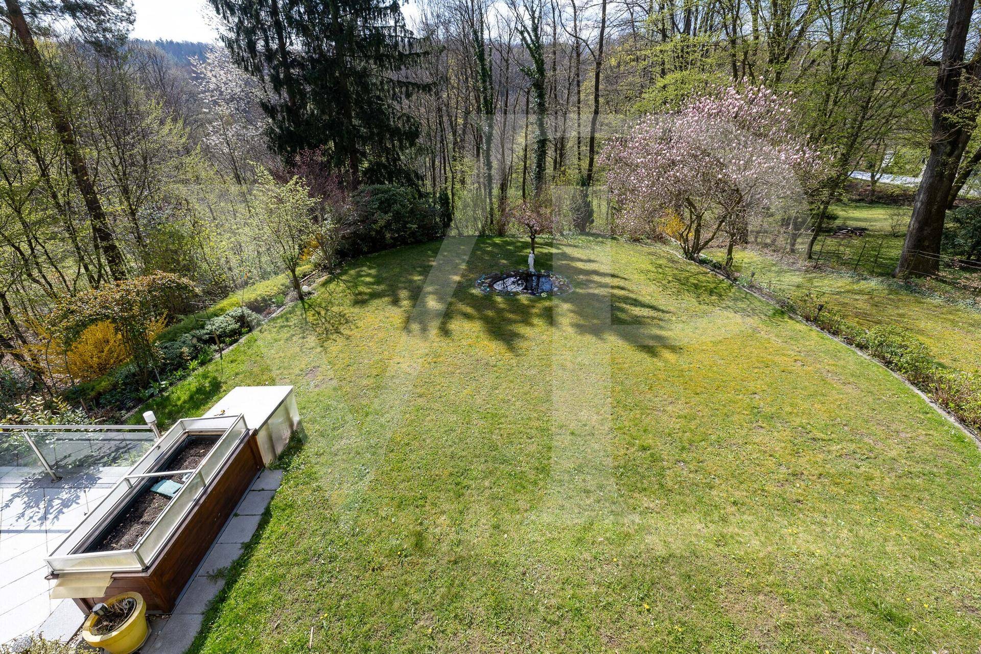 Weitläufige Rasenfläche des Gartens mit altem Baumbestand und Blick auf die Umgebung.