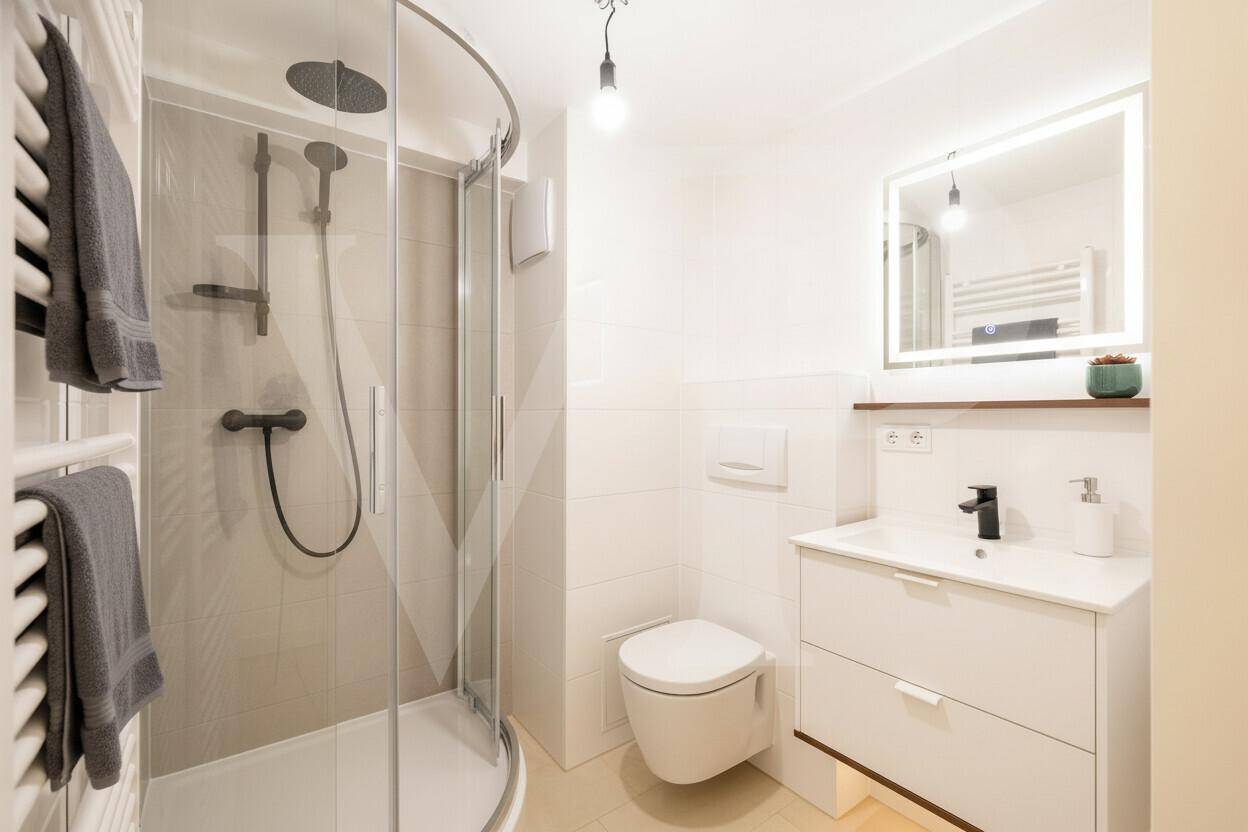 Helles Badezimmer mit Duschkabine, modernem Waschtisch und beheiztem Handtuchhalter in Weiß.