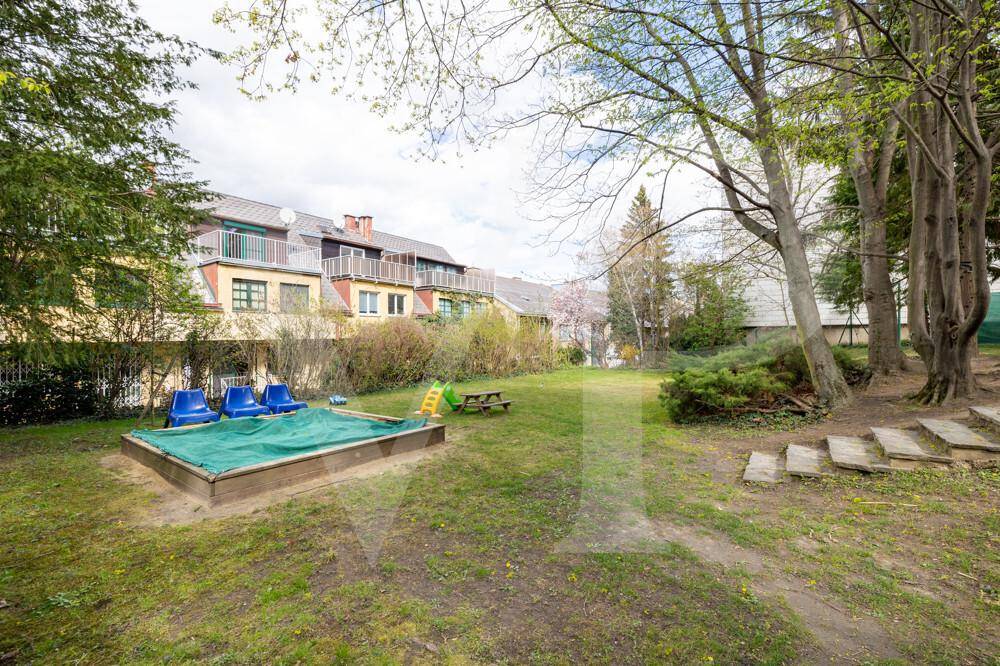 Gartenbereich mit Sandkasten, Bäumen und Blick auf die angrenzenden Gebäude.