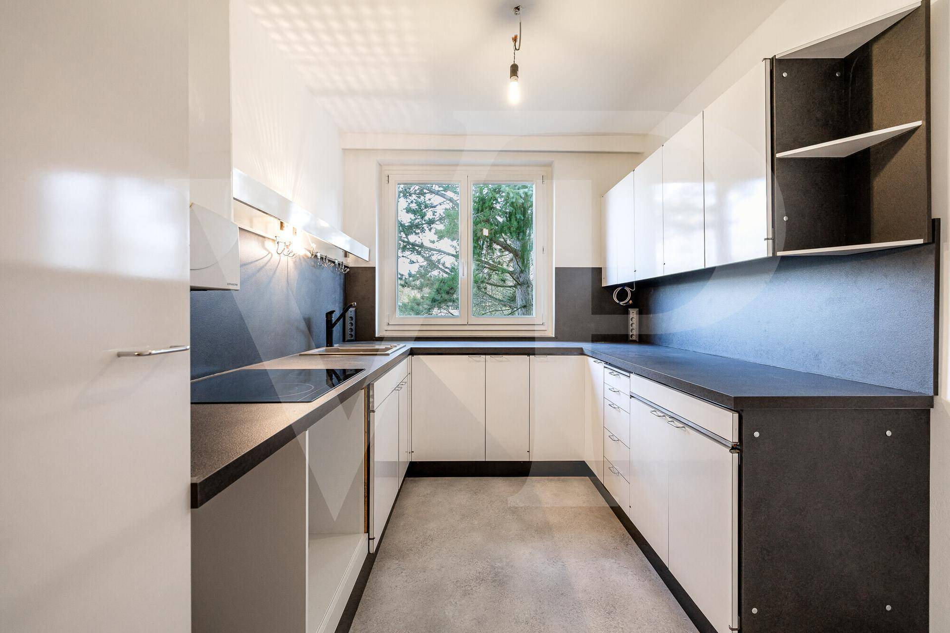 Funktionale Küche mit weißen Schränken, dunklen Arbeitsplatten und Fensterblick ins Grüne.