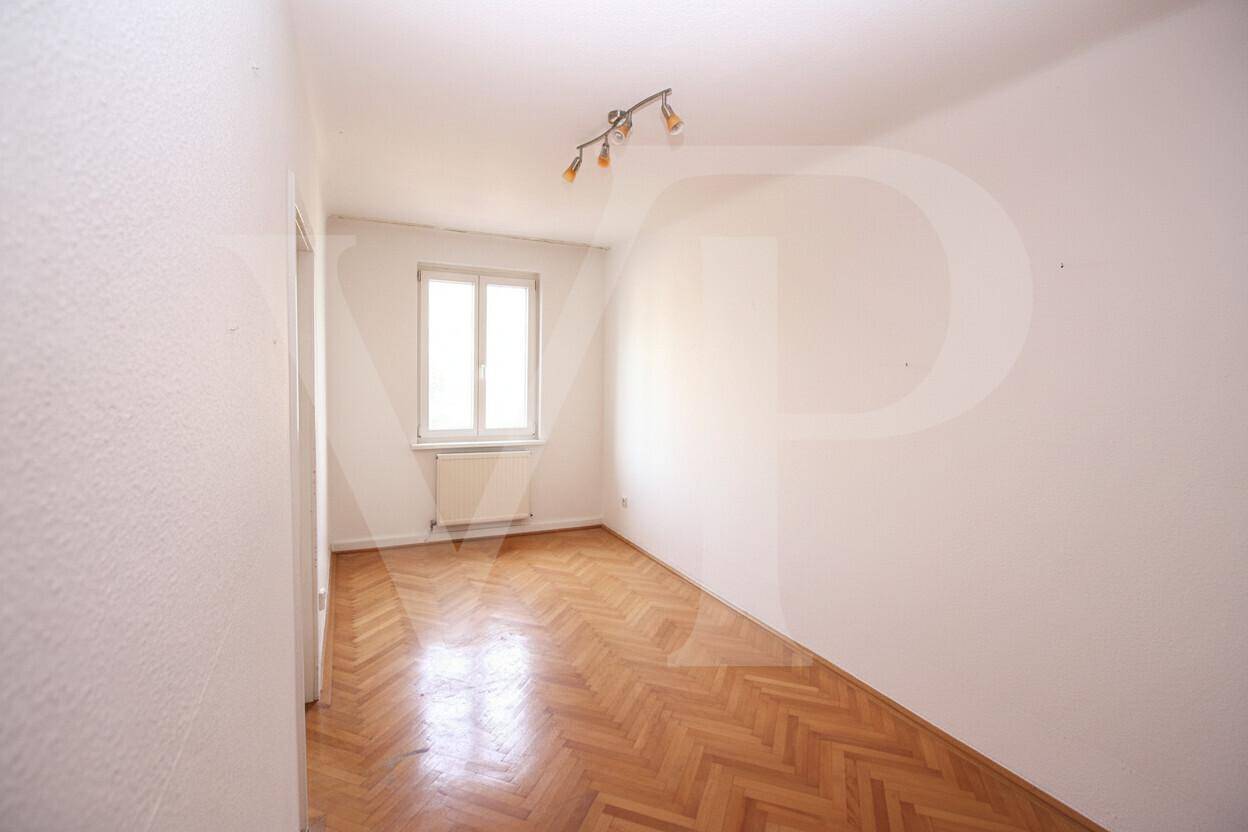 Helles, leeres Schlafzimmer mit weißen Wänden und klassischem Fischgrätparkett.
