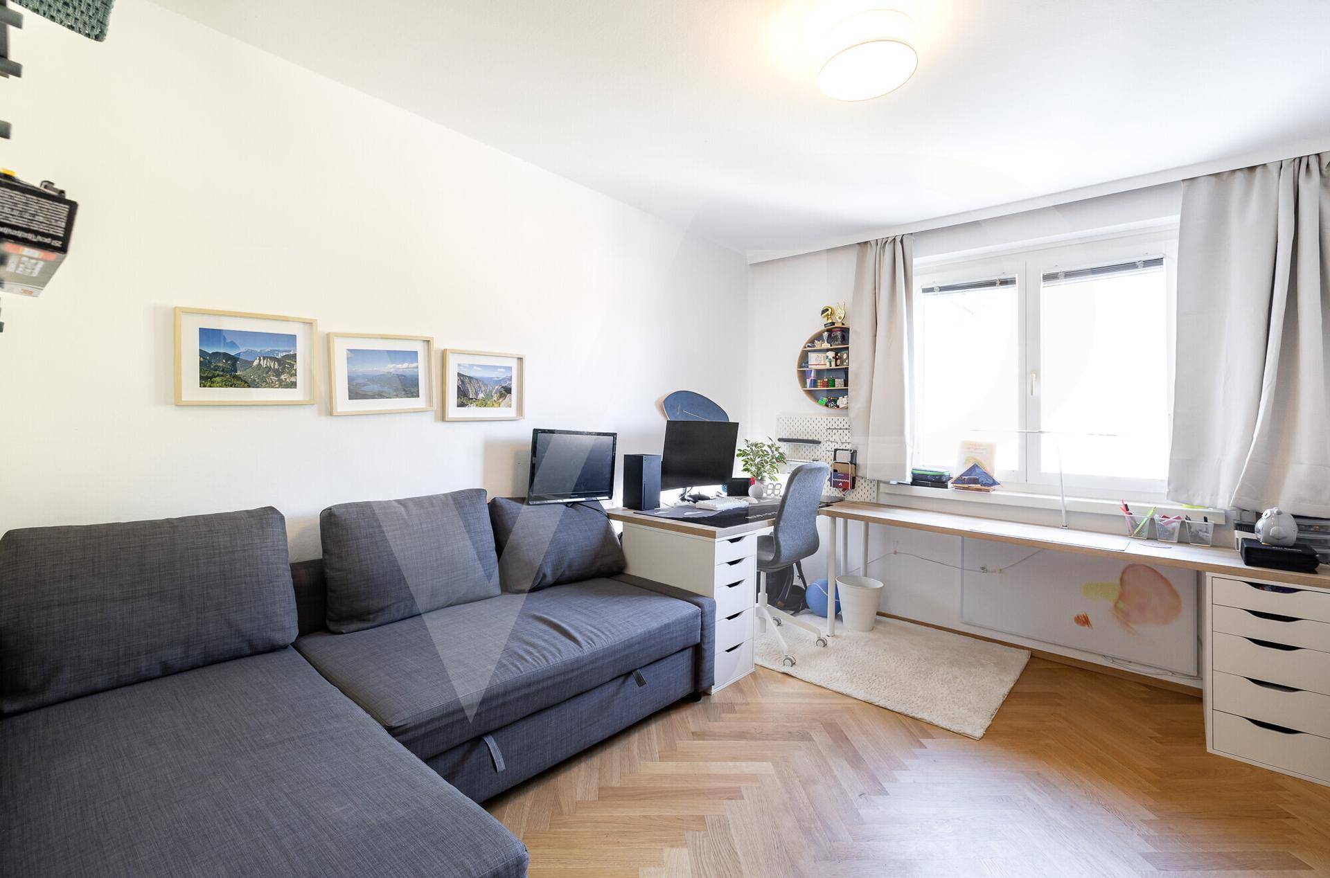 Helles Arbeitszimmer mit großem Schreibtisch, Sofa und Fischgrätparkett, ideal für Home-Office.