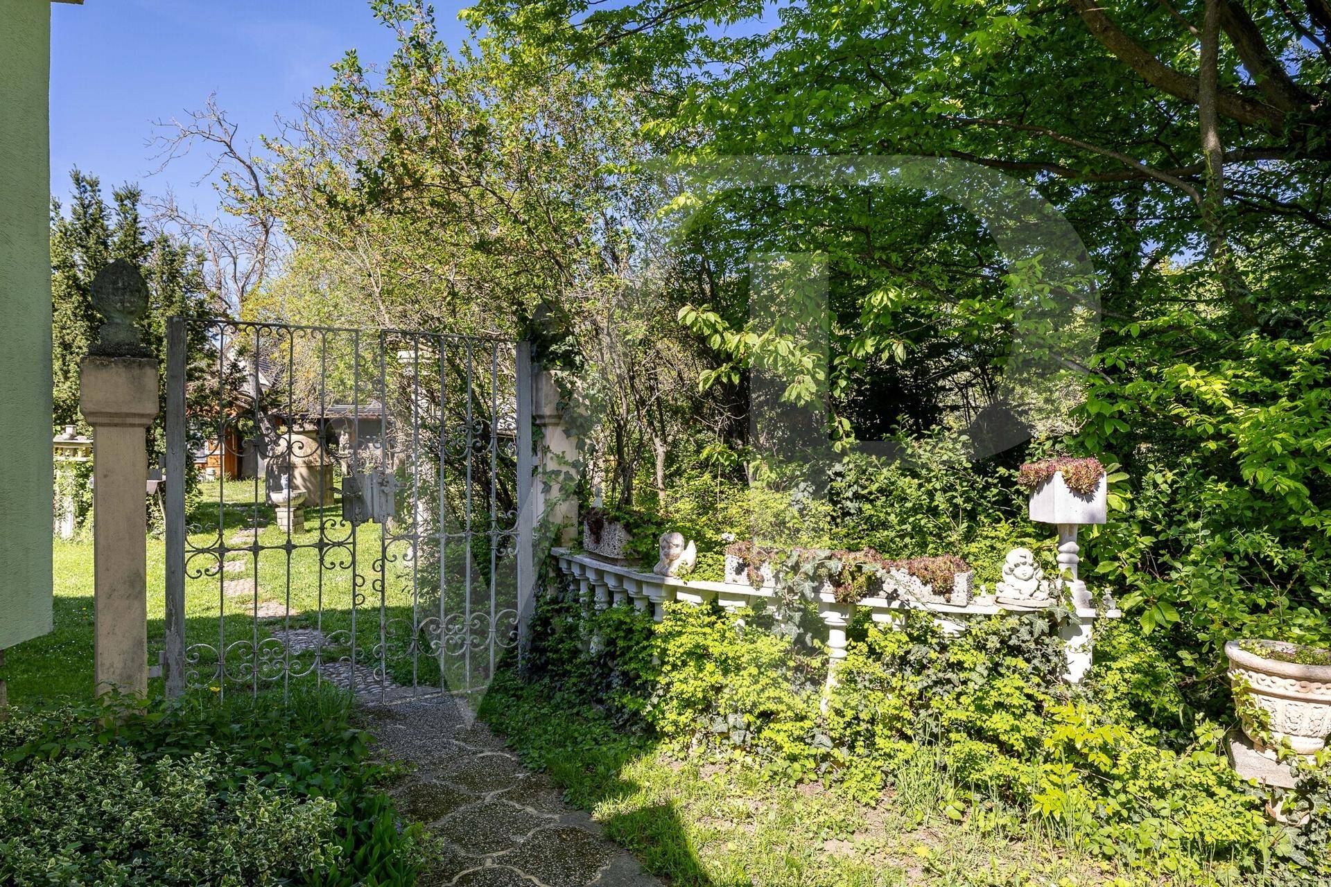 Historisches Gartentor mit Steinpfosten und üppiger Bepflanzung, die einen verwunschenen Gartenweg säumt.
