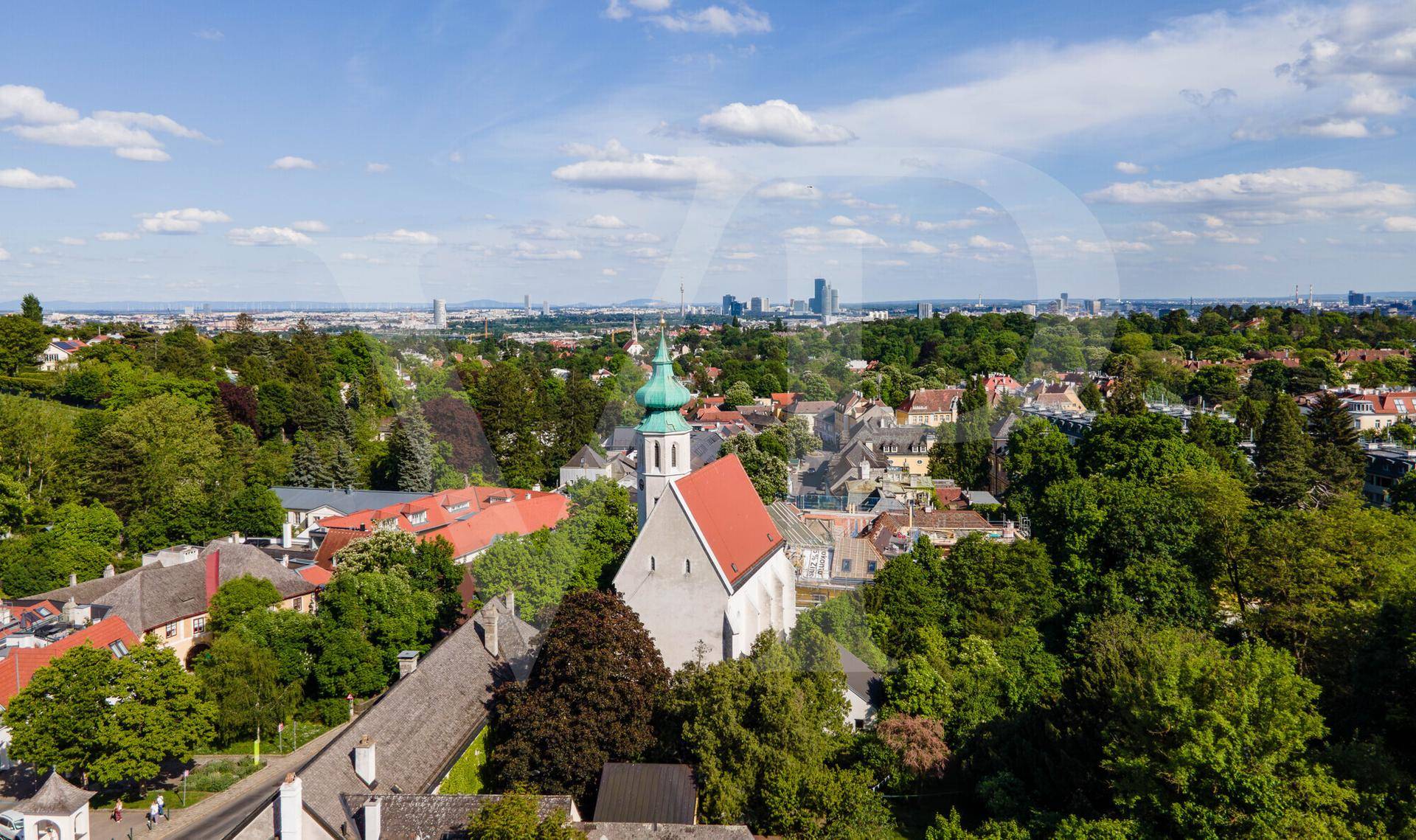 Panoramablick über eine charmante Stadt mit Kirche, grünen Bäumen und einer fernen Skyline.