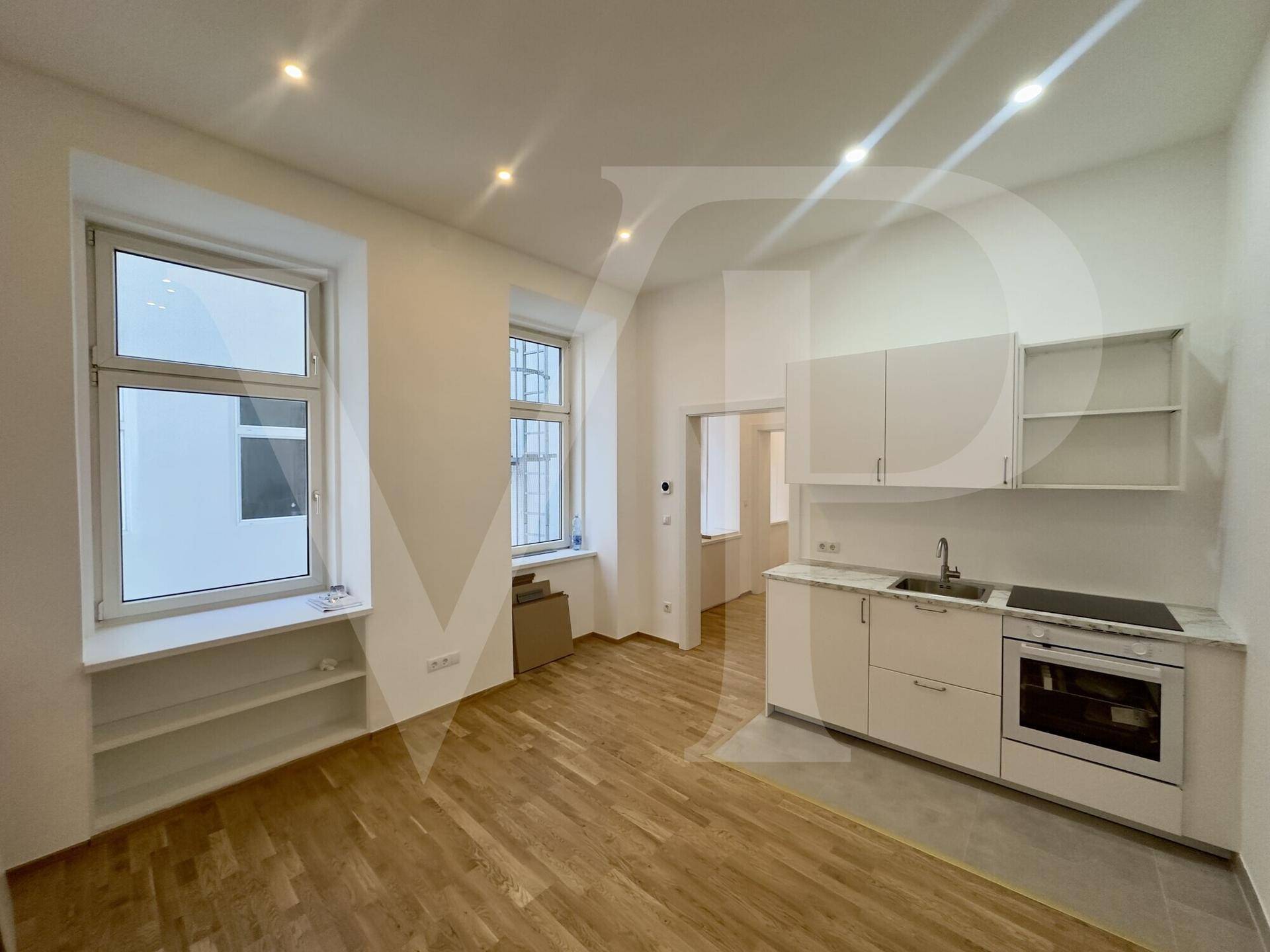 Heller Raum mit integrierter Küchenzeile, Holzboden und großen Fenstern.