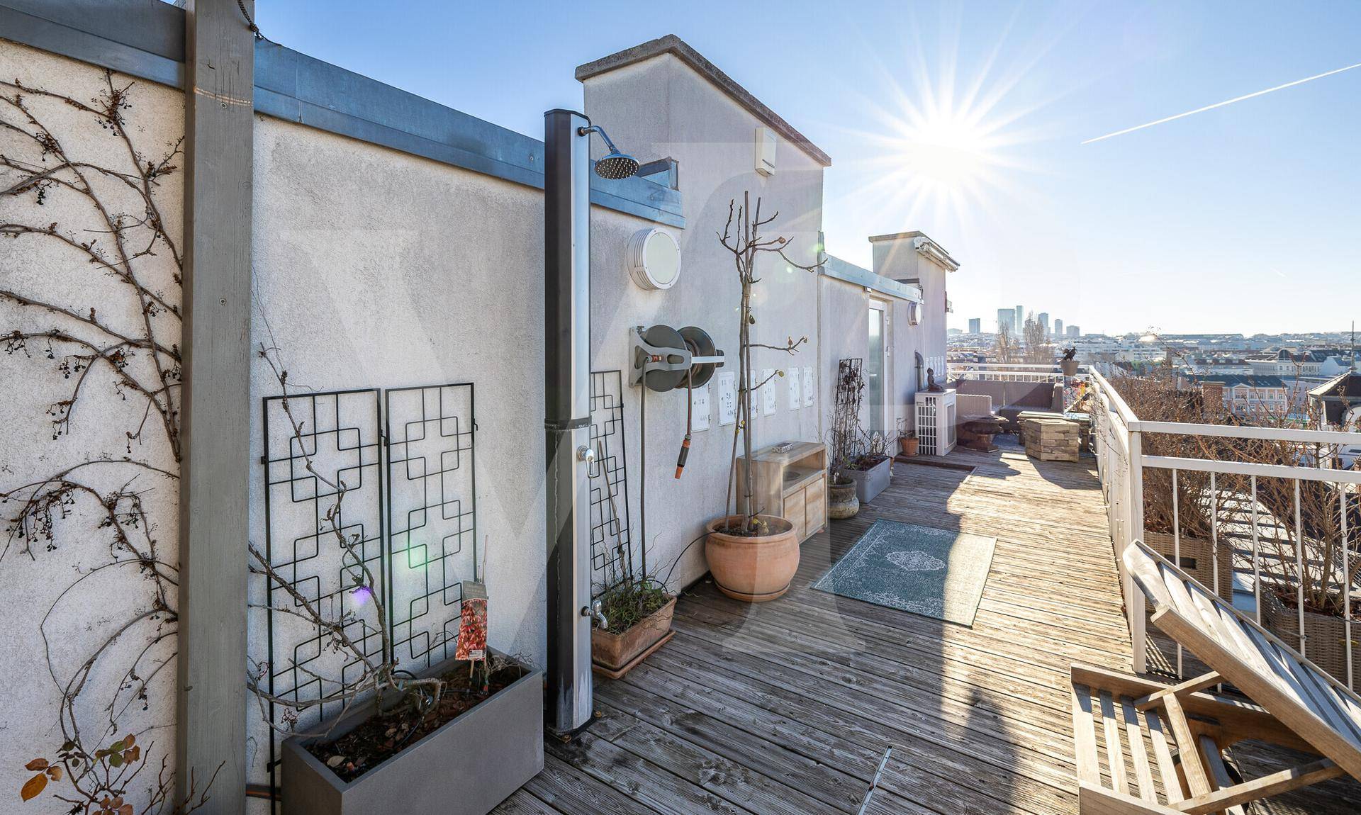 Weitläufige Dachterrasse mit Holzbelag, Außendusche und Panoramablick über die Dächer der Stadt.