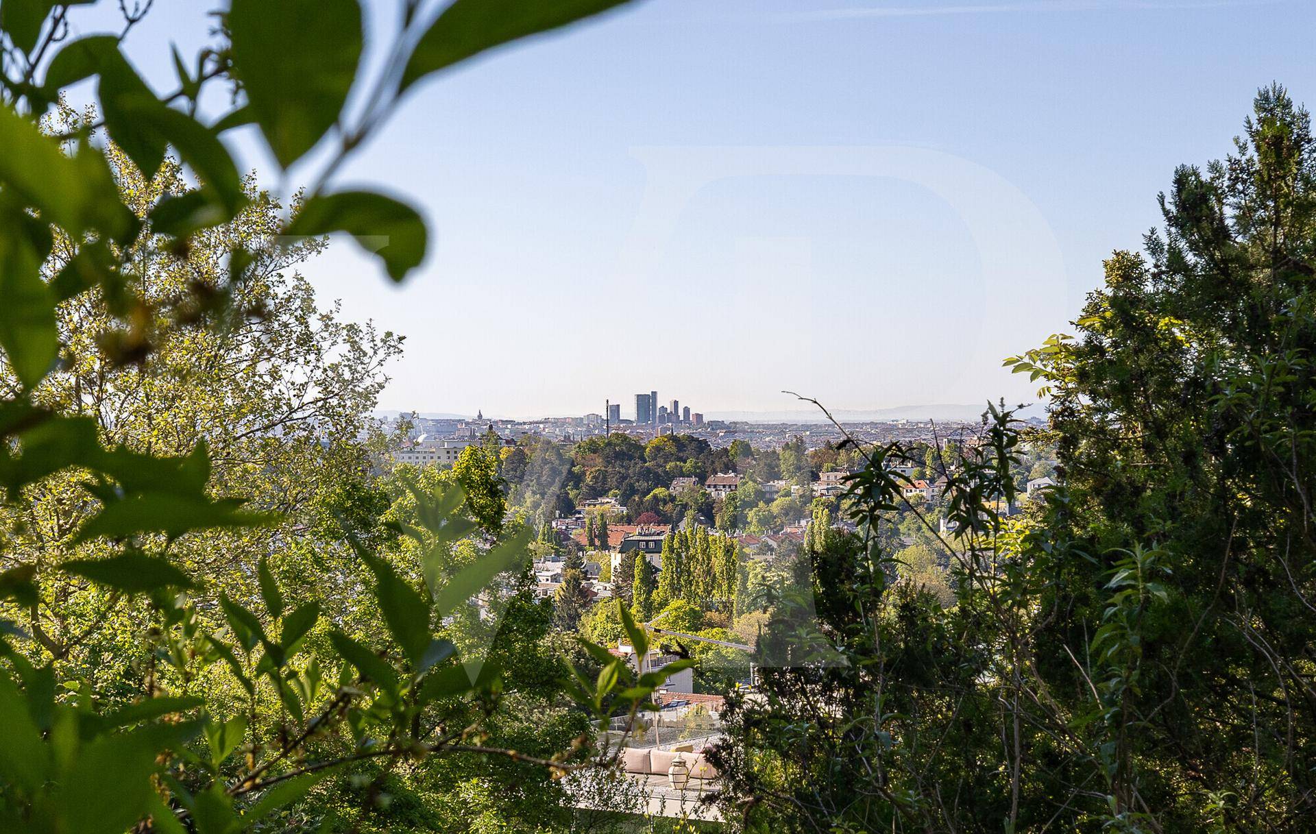 Panoramablick auf die Stadtkulisse durch die Blätter der Bäume, mit Hochhäusern am Horizont.
