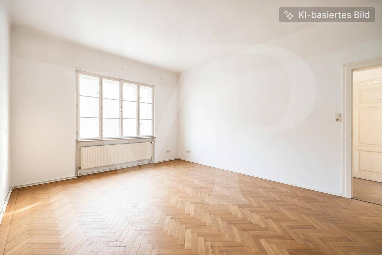 Leeres Zimmer mit Fischgrätparkettboden und einem großen Fenster, das viel Tageslicht hereinlässt.