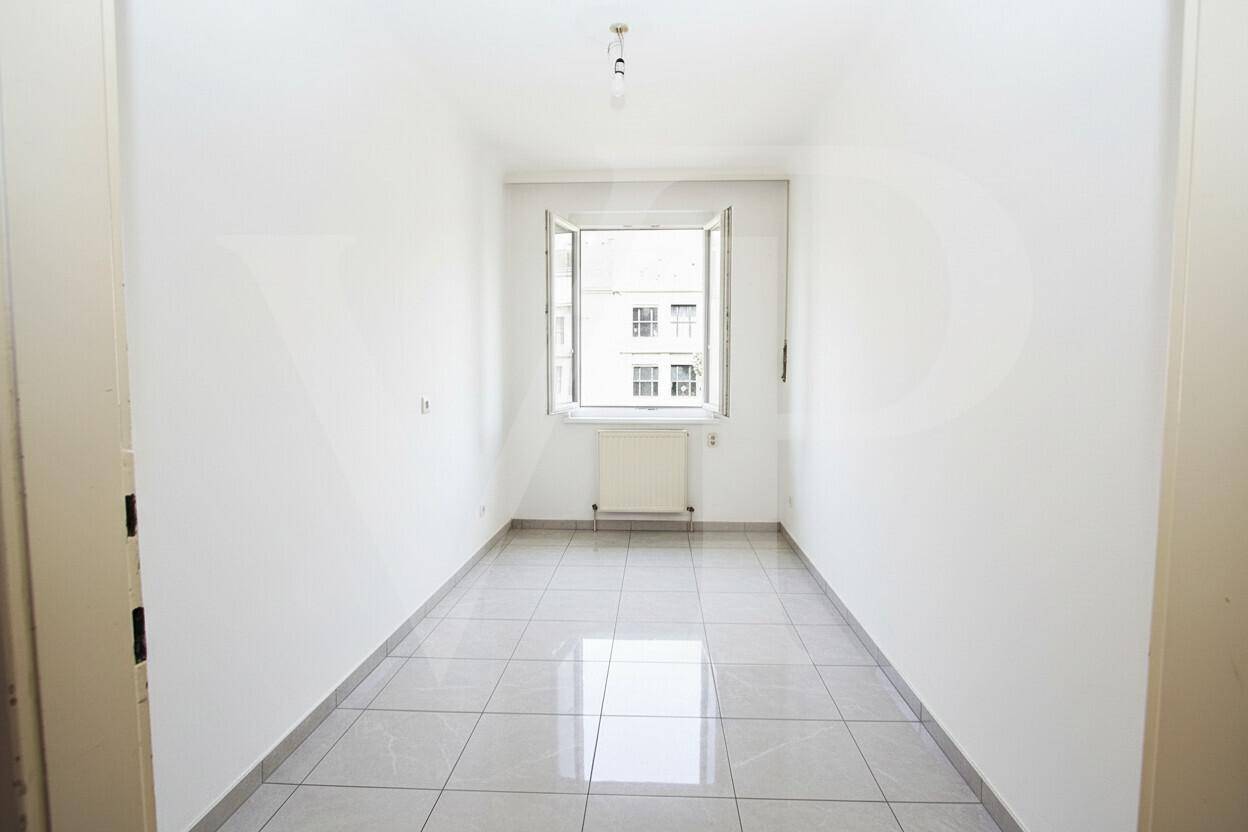 Heller, leerer Raum mit modernen grauen Fliesen und einem Fenster.