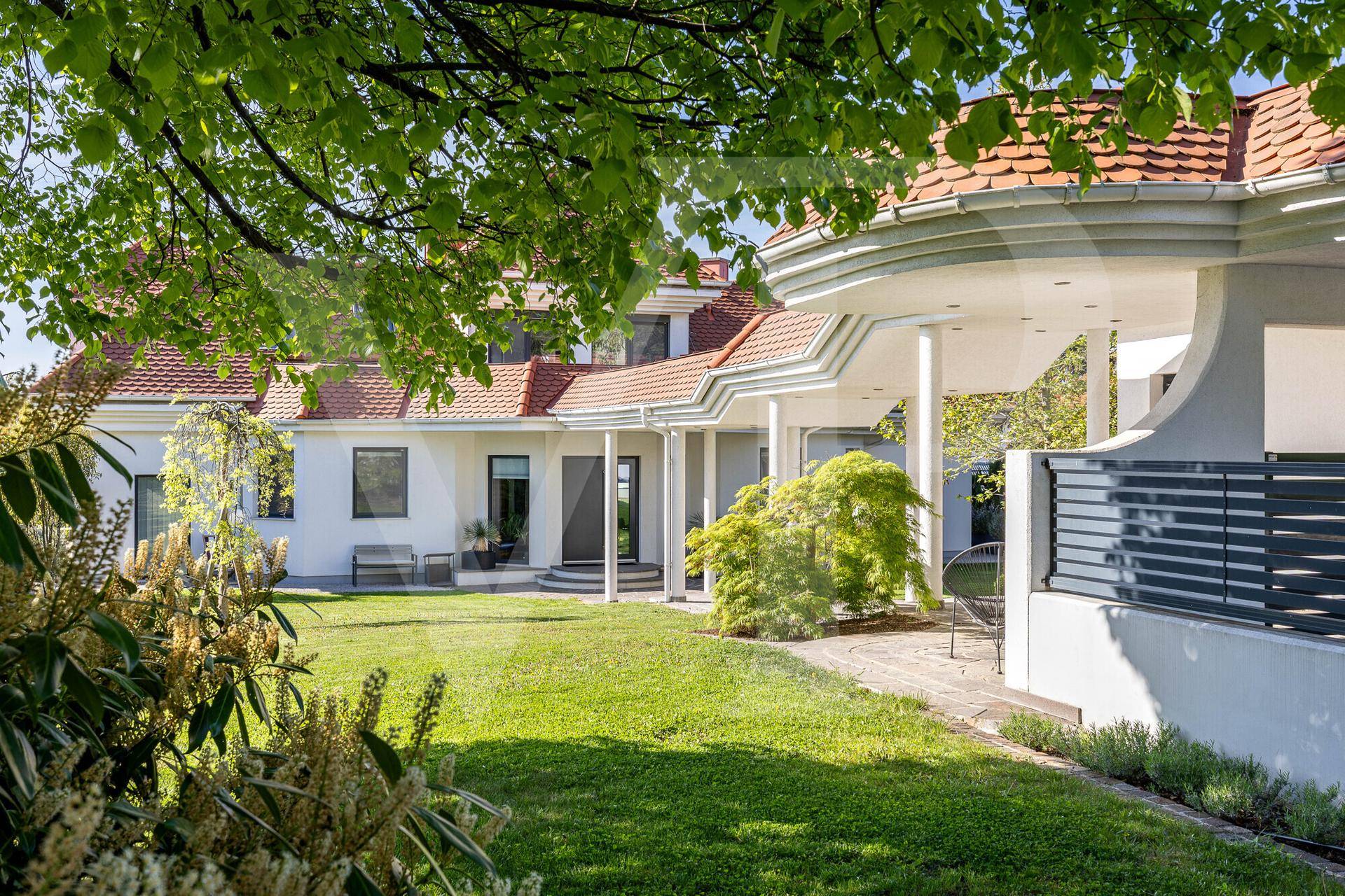 Gepflegter Gartenbereich mit Rasenfläche, Bäumen und Blick auf die moderne Villa.