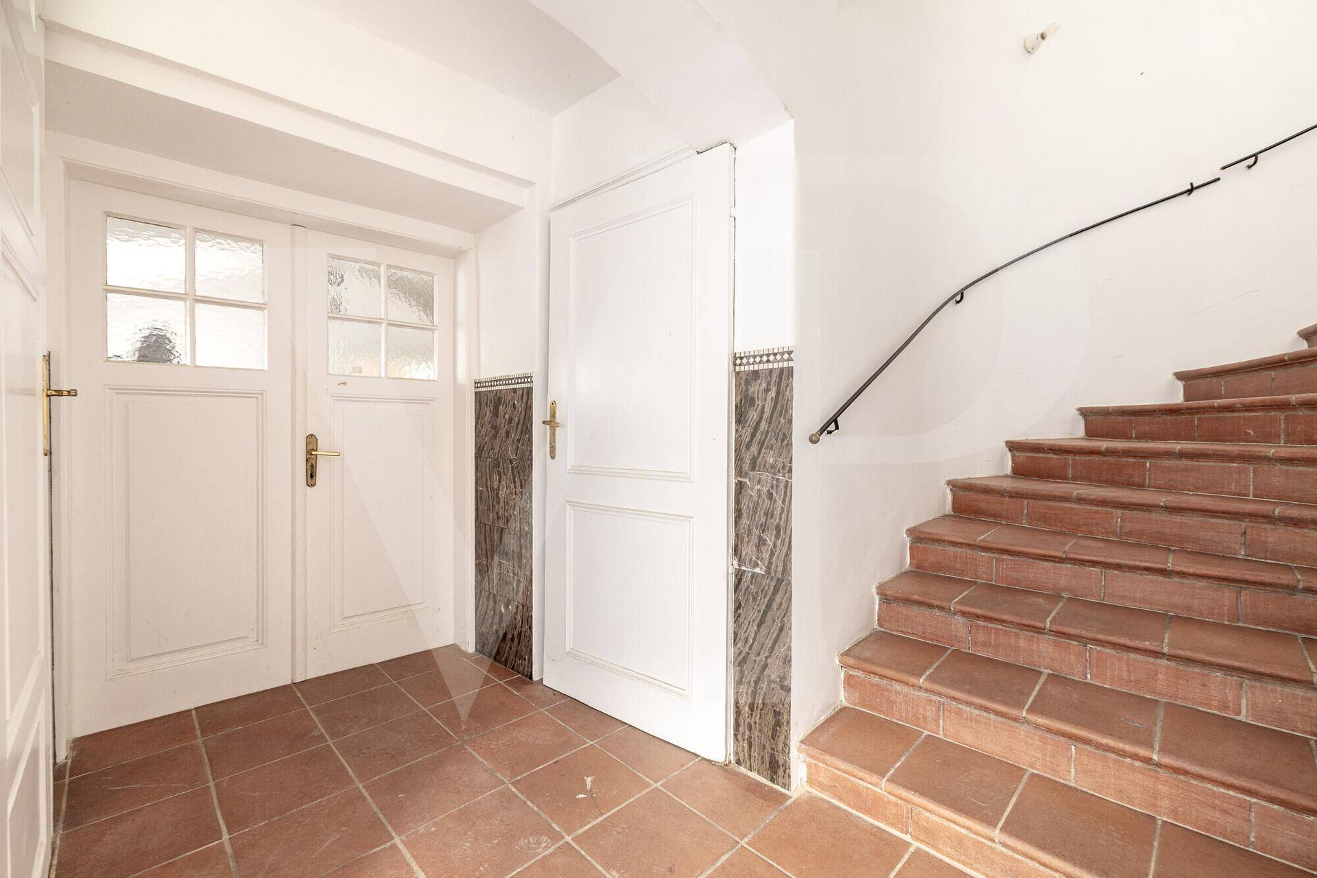 Heller Eingangsbereich mit Terrakotta-Fliesenboden und einer geschwungenen Treppe mit Marmorakzenten.