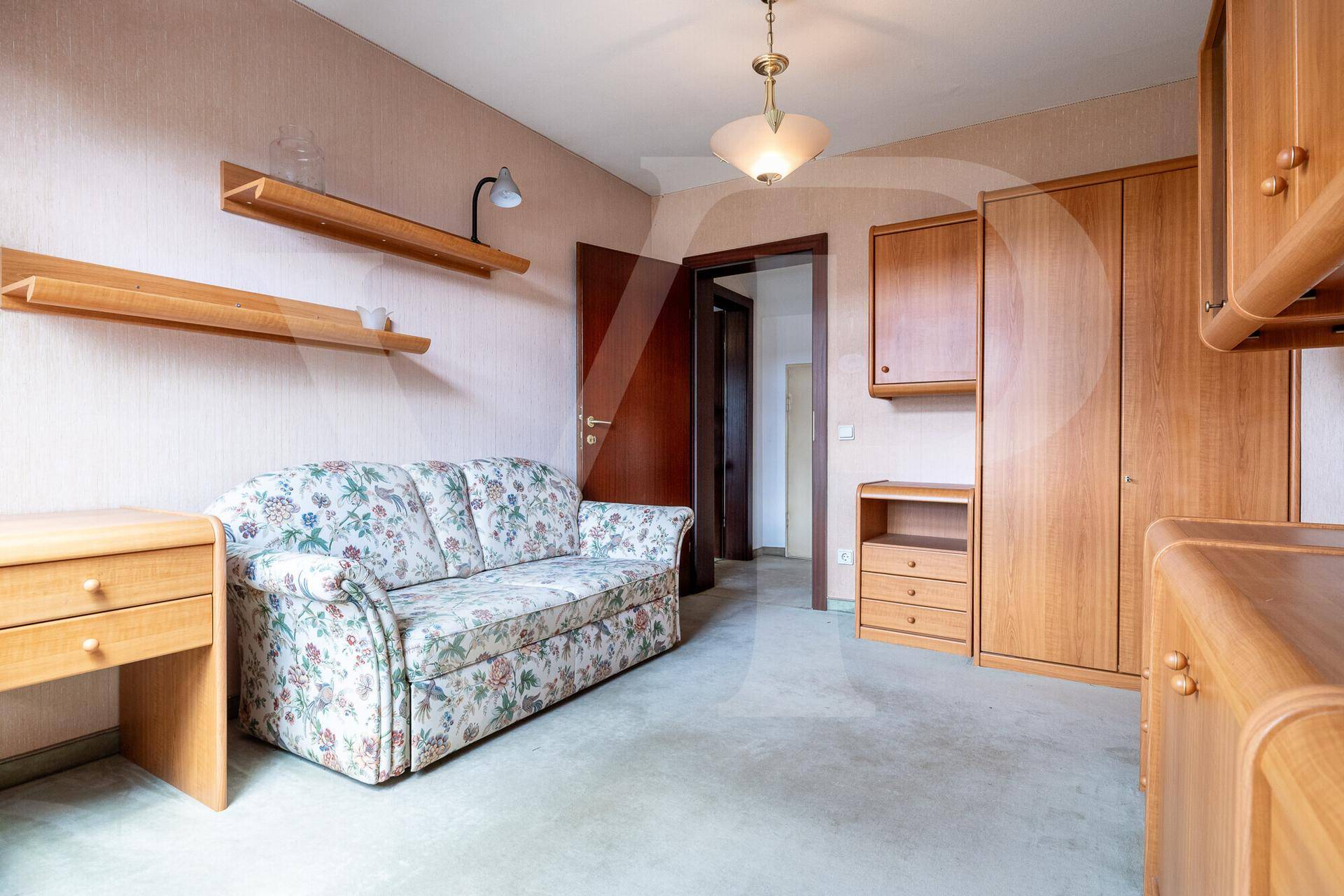 Gemütliches Dachzimmer mit schräger Decke, floralem Sofa und praktischen Holzmöbeln.