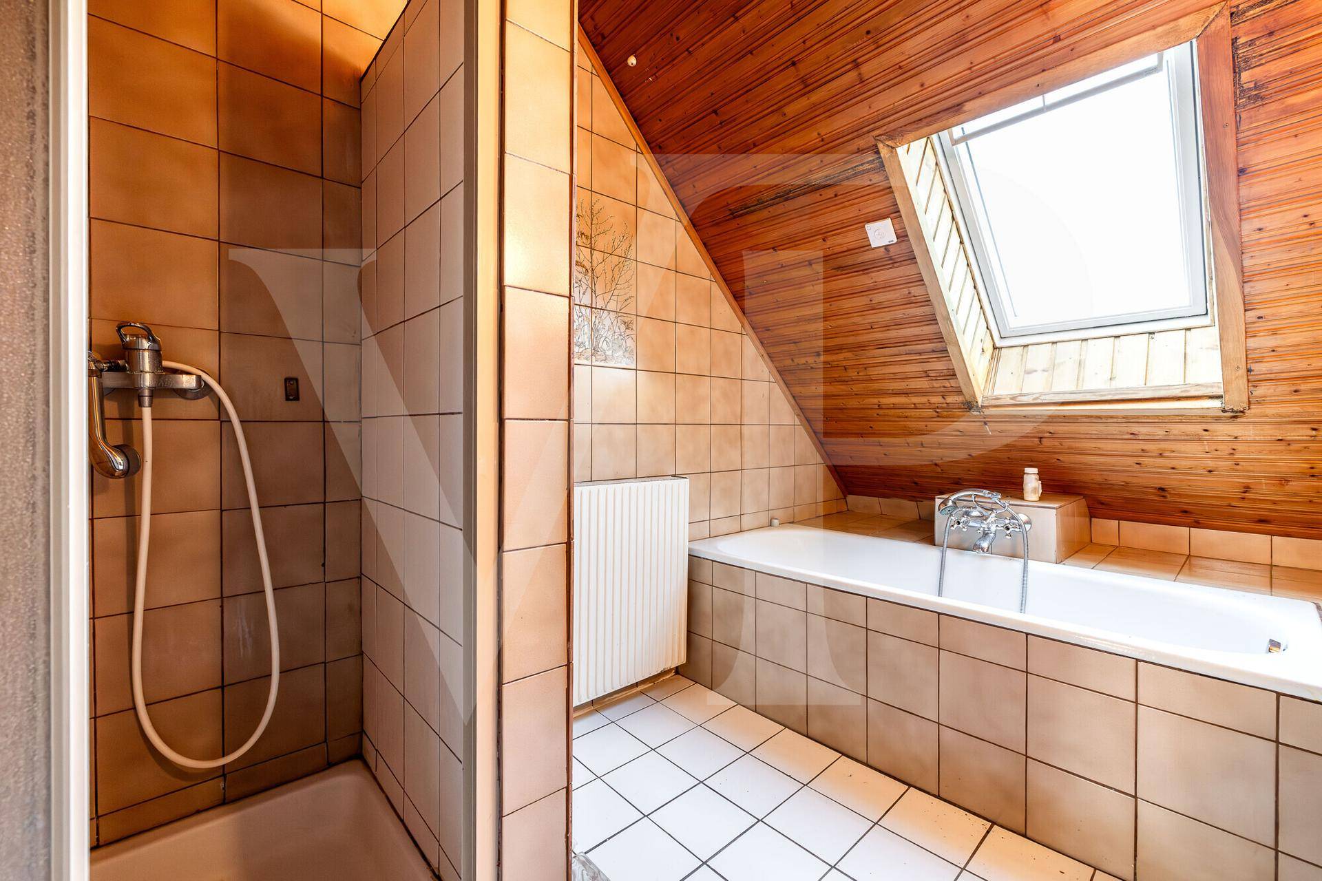 Badezimmer im Dachgeschoss mit Badewanne, Dusche, Dachfenster und Holzverkleidung.