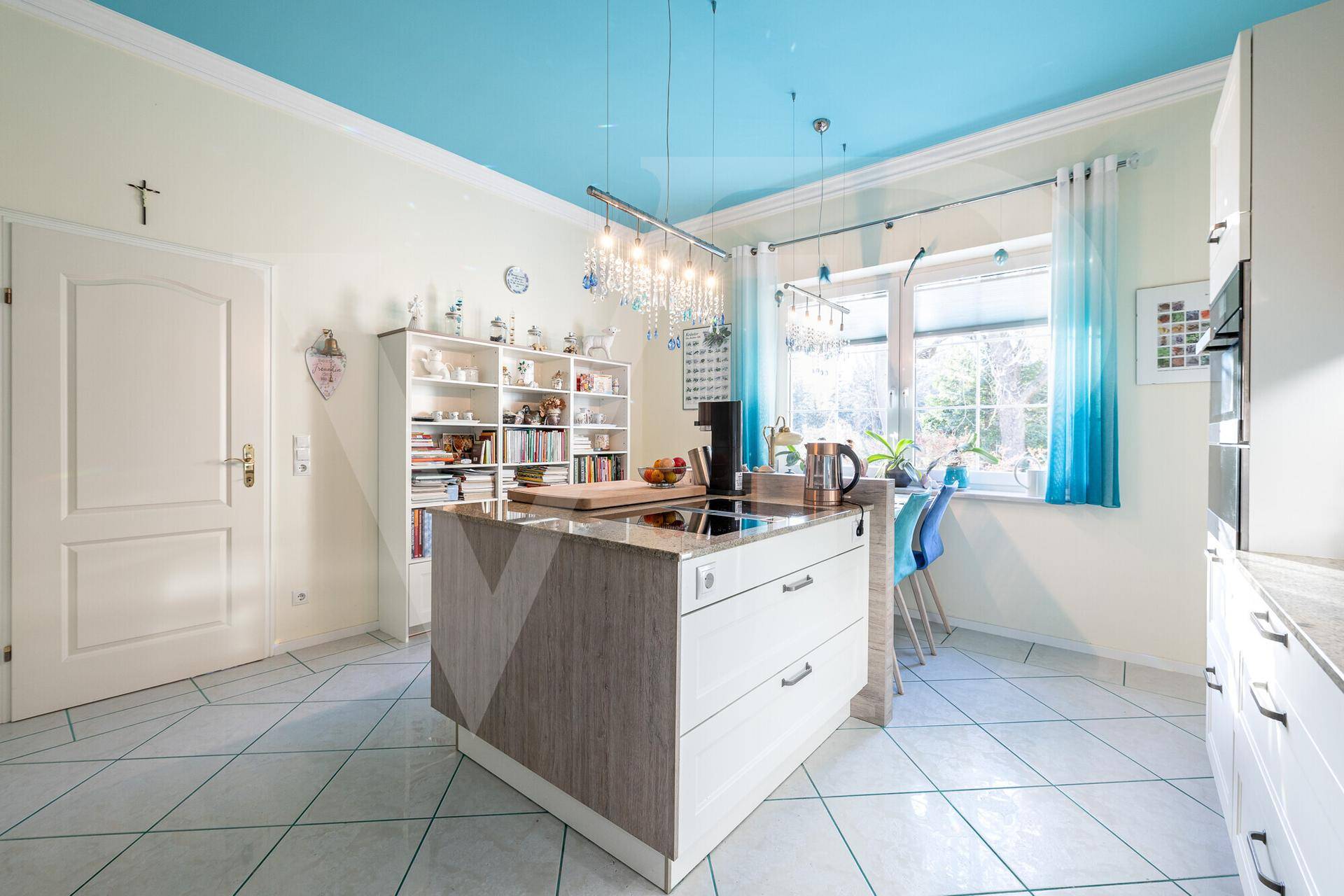 Helle Küche mit blauer Decke, Kücheninsel und Fensterblick ins Grüne.