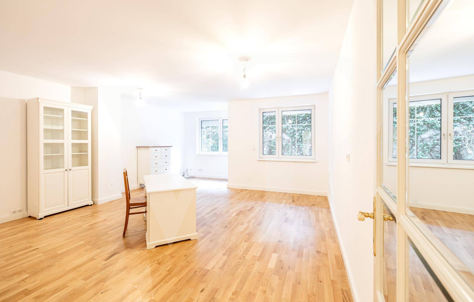 Geräumiges Zimmer mit Holzboden, großen Fenstern und einem Schreibtisch, vielseitig nutzbar.