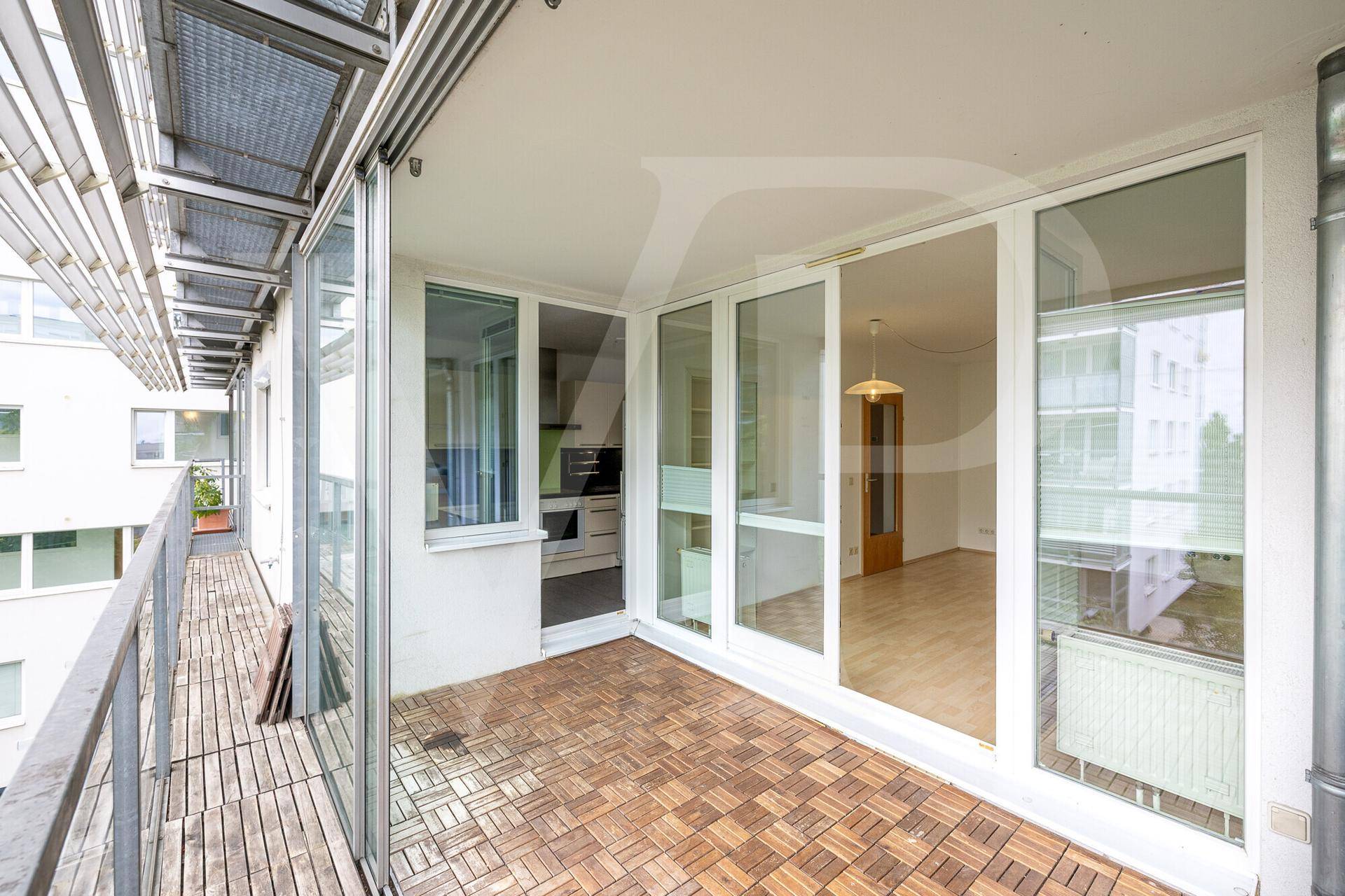 Geräumige Loggia mit Holzboden und großen Glasfronten, die Zugang zum Wohnbereich bietet.