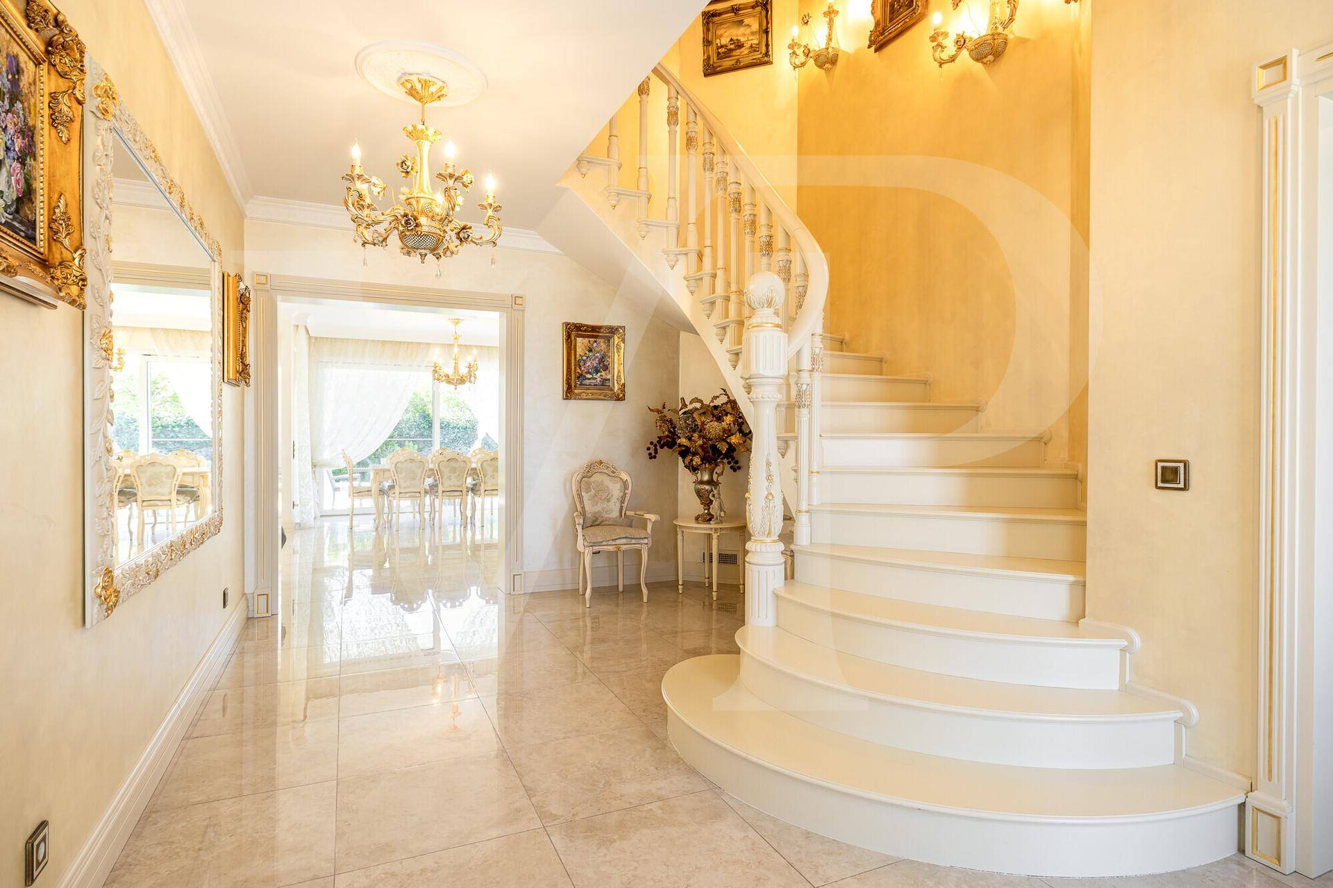 Repräsentativer Eingangsbereich mit geschwungener Treppe, glänzenden Fliesen und opulenten Wandleuchten.
