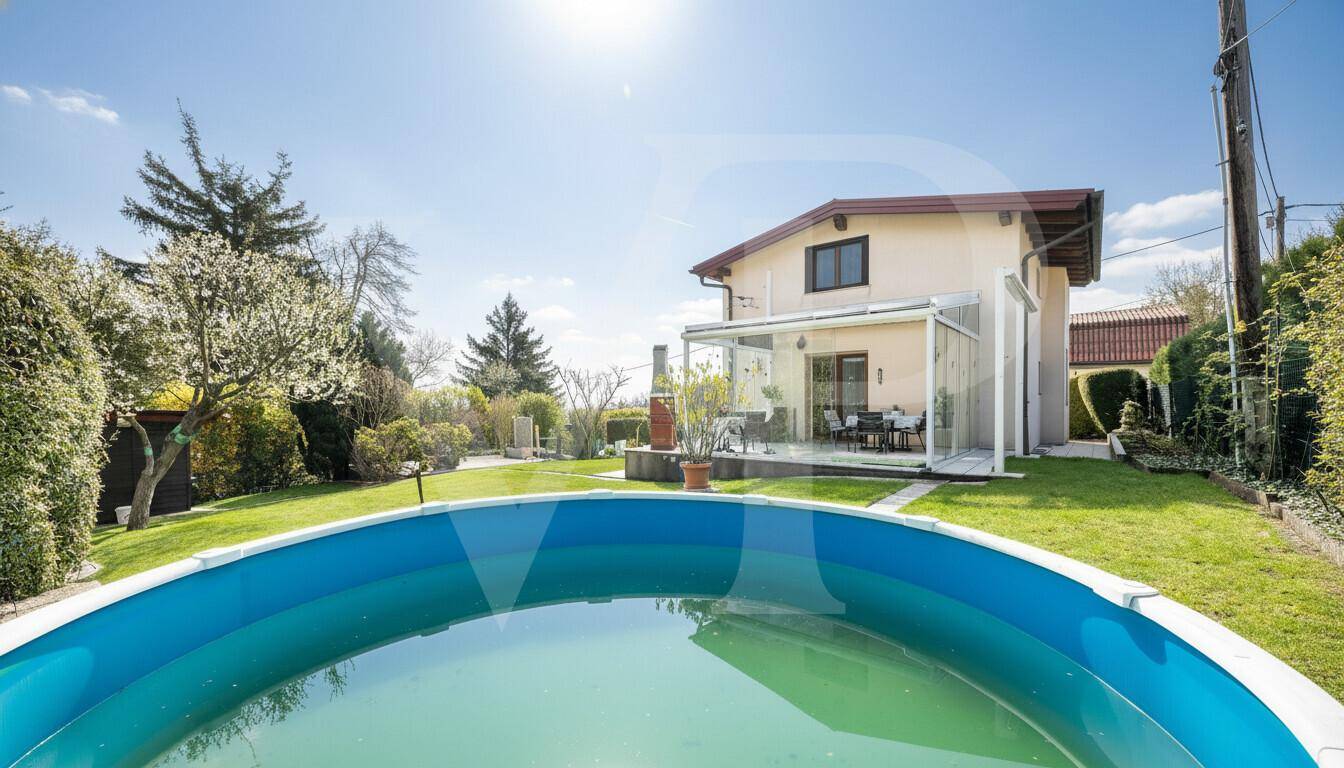 Hausfassade mit großem Garten, Pool und verglastem Wintergarten unter blauem Himmel.