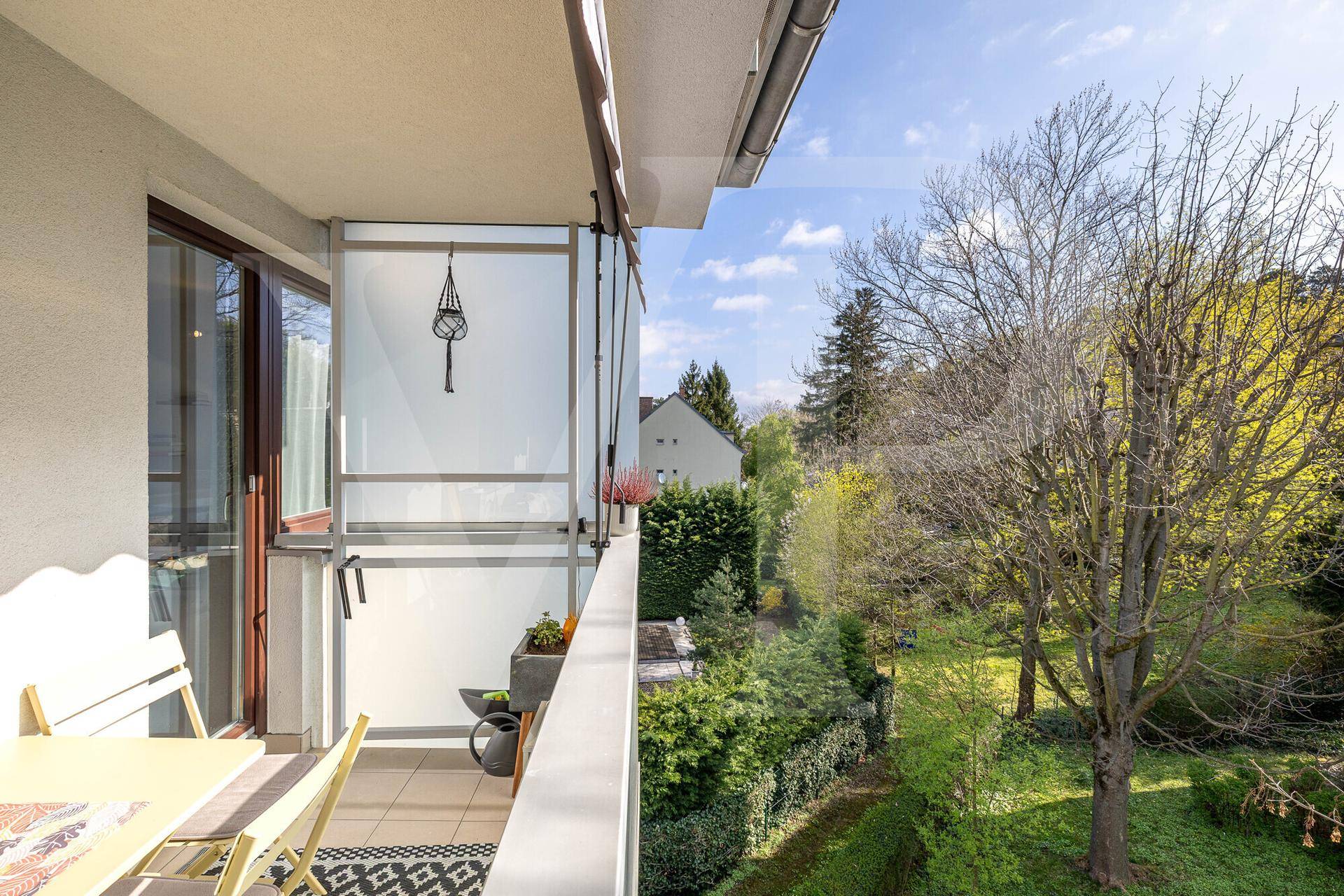 Heller Balkon mit Blick ins Grüne und auf die umliegende Natur, mit Glasabtrennung.