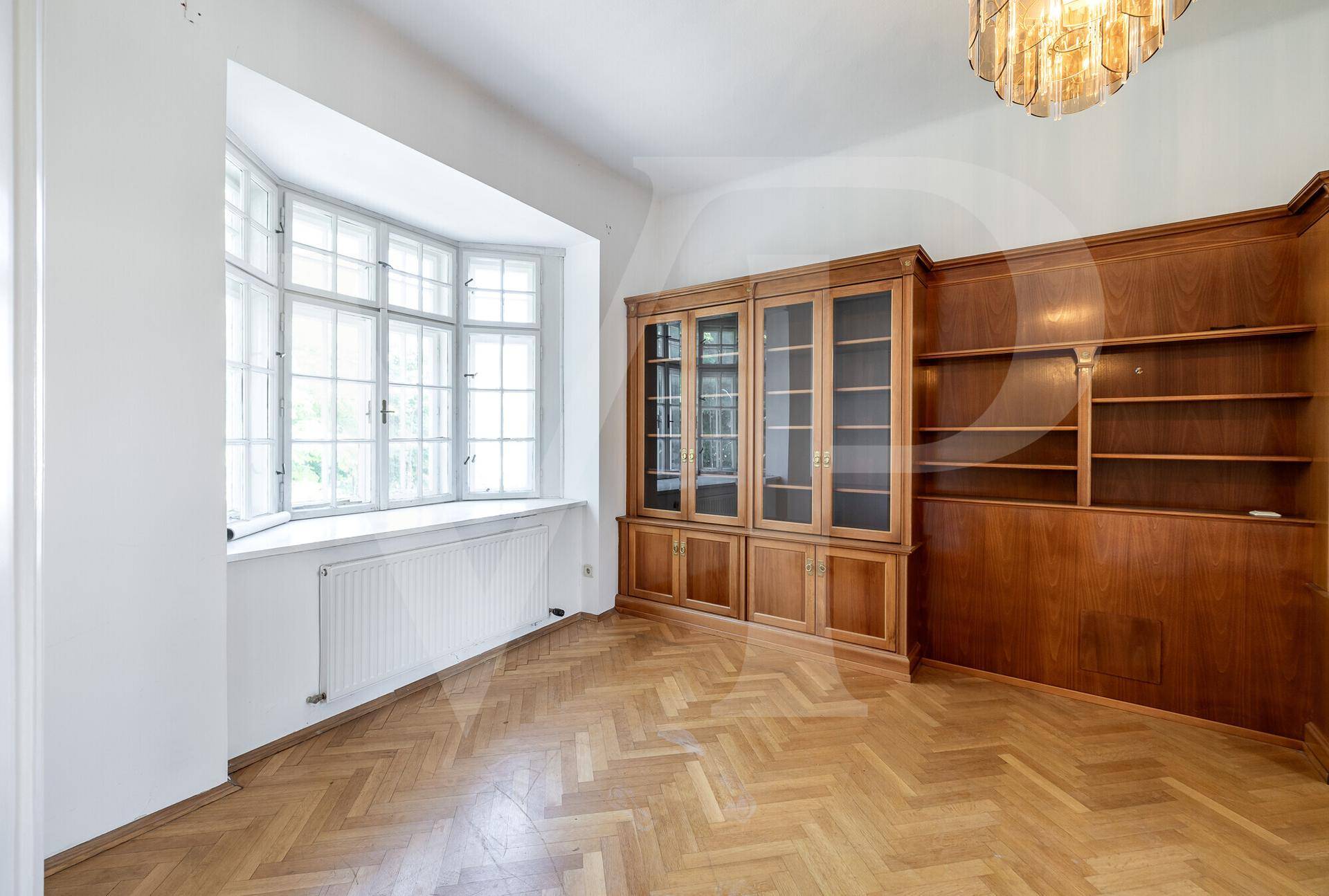 Zimmer mit Fischgrätparkett, Erkerfenster und eleganten, eingebauten Holzregalen.