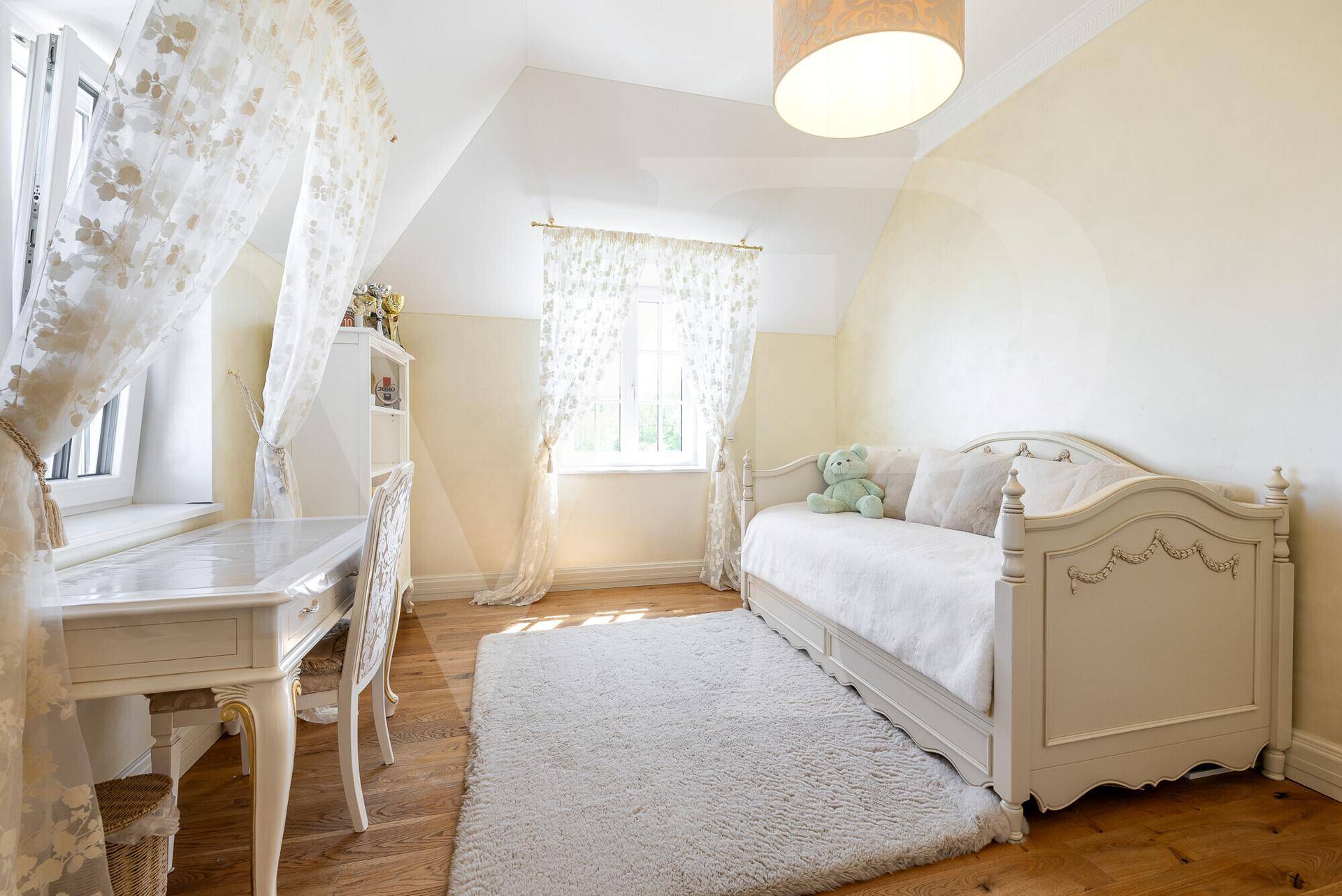 Freundliches Kinderzimmer mit Holzboden, weißem Bett und Schreibtisch unter Dachschräge.