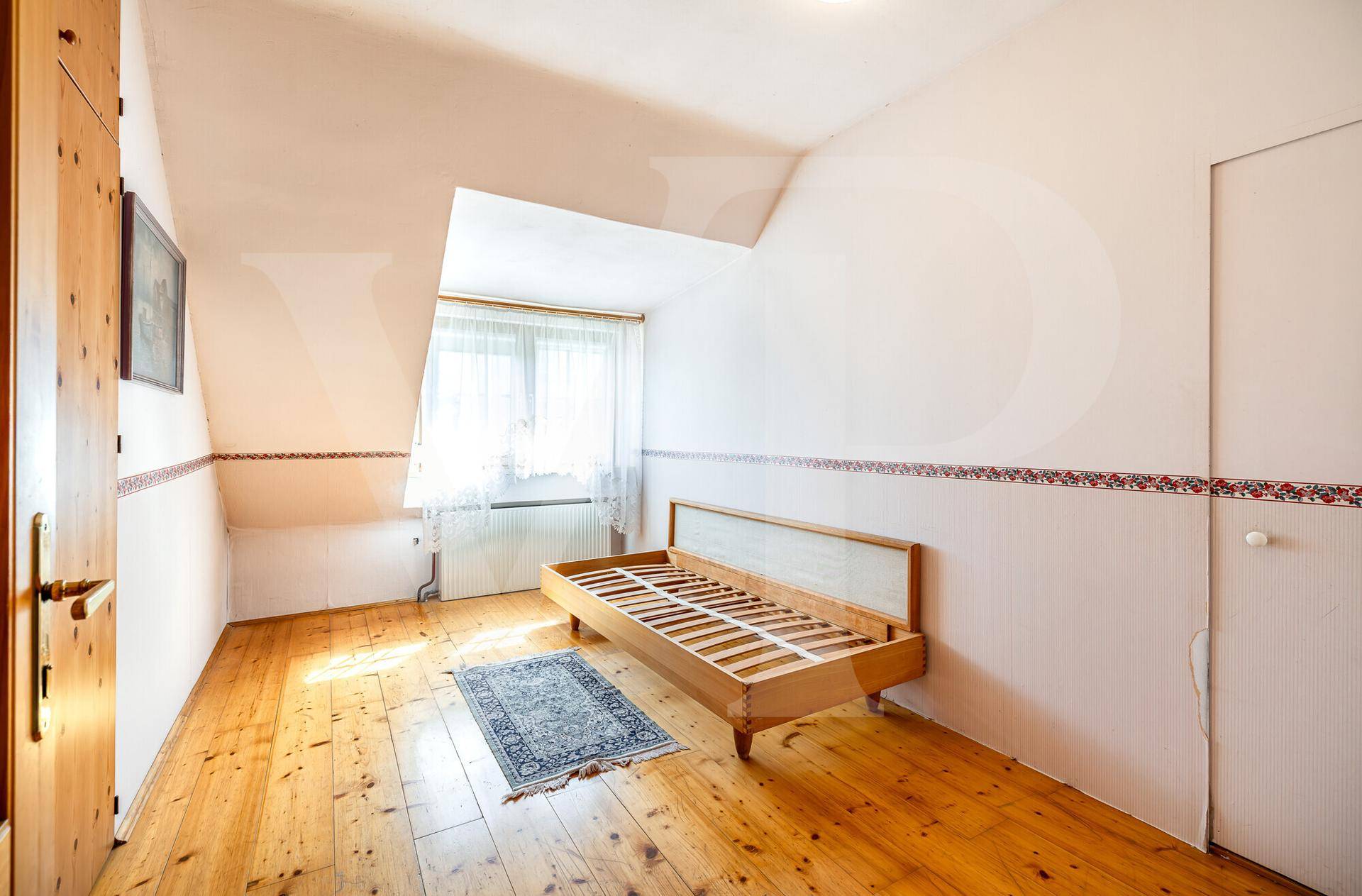 Schlafzimmer im Dachgeschoss mit Holzboden, Dachschräge und einem Bettgestell.