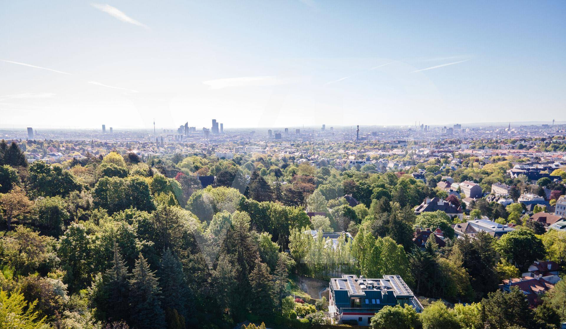 Panoramablick über eine grüne Stadtlandschaft mit Hochhäusern am Horizont und vielen Bäumen.