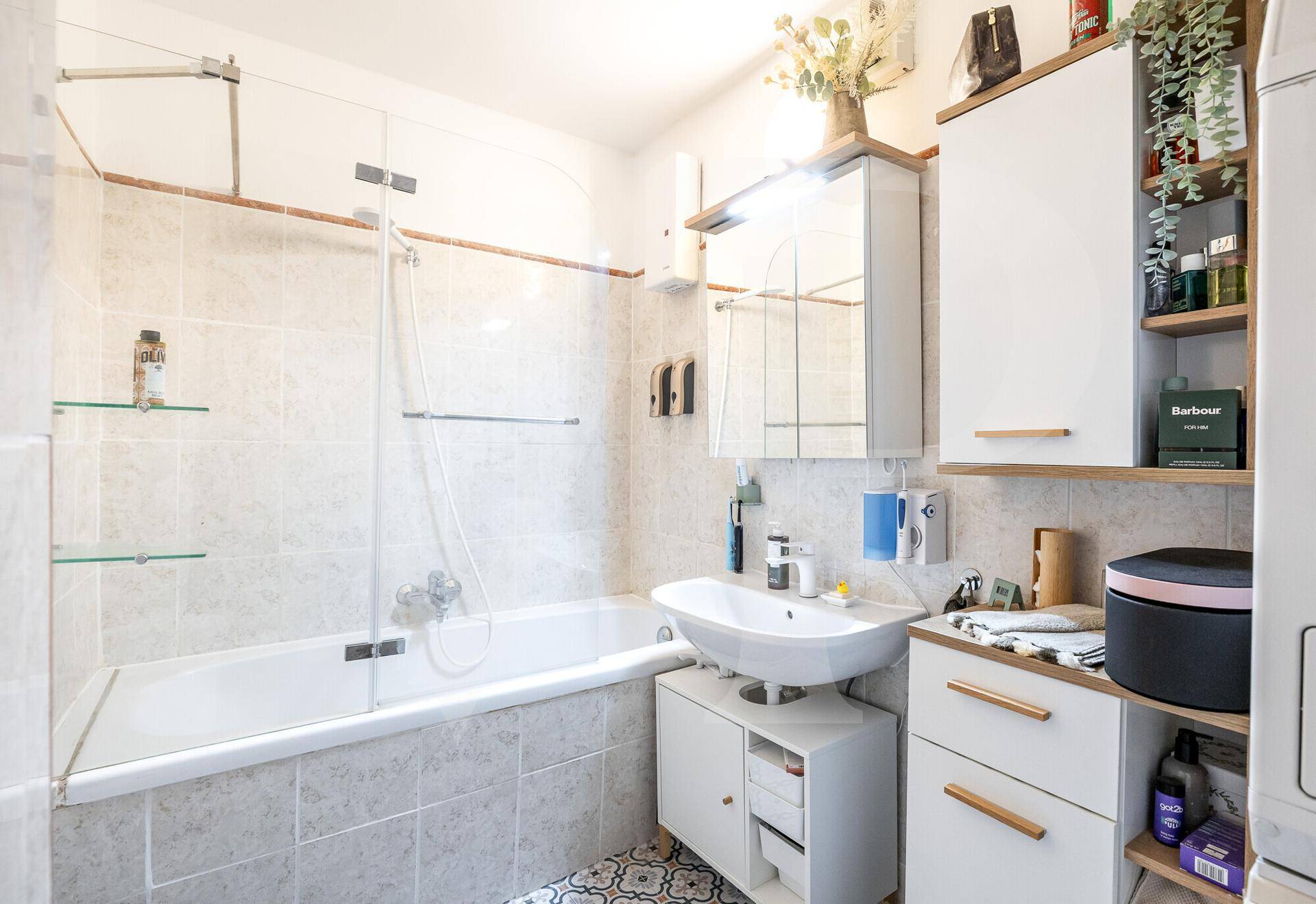 Badezimmer mit Badewanne, Duschabtrennung und Waschbecken, hell gefliest und funktional.