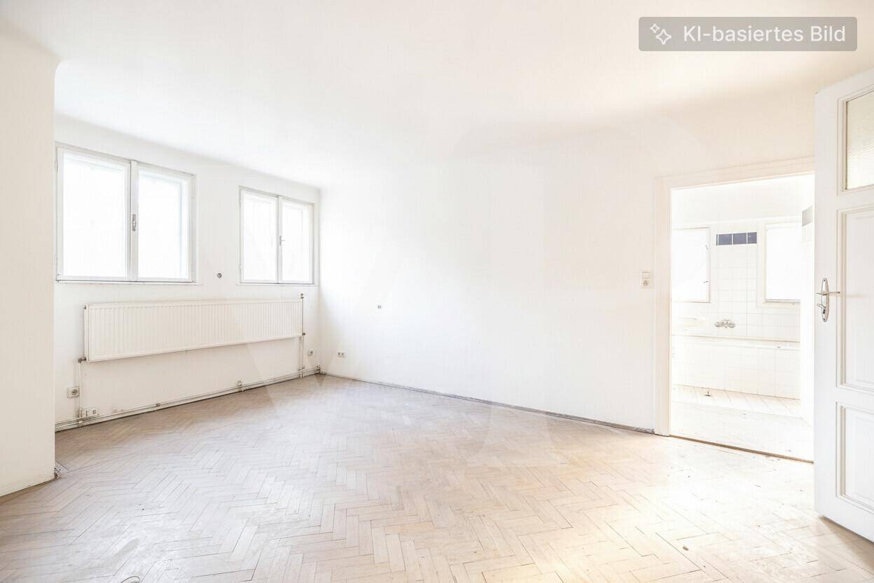 Helles Zimmer mit hellem Fischgrätparkett, weißen Wänden und zwei Fenstern, mit Zugang zu einem Nebenraum.