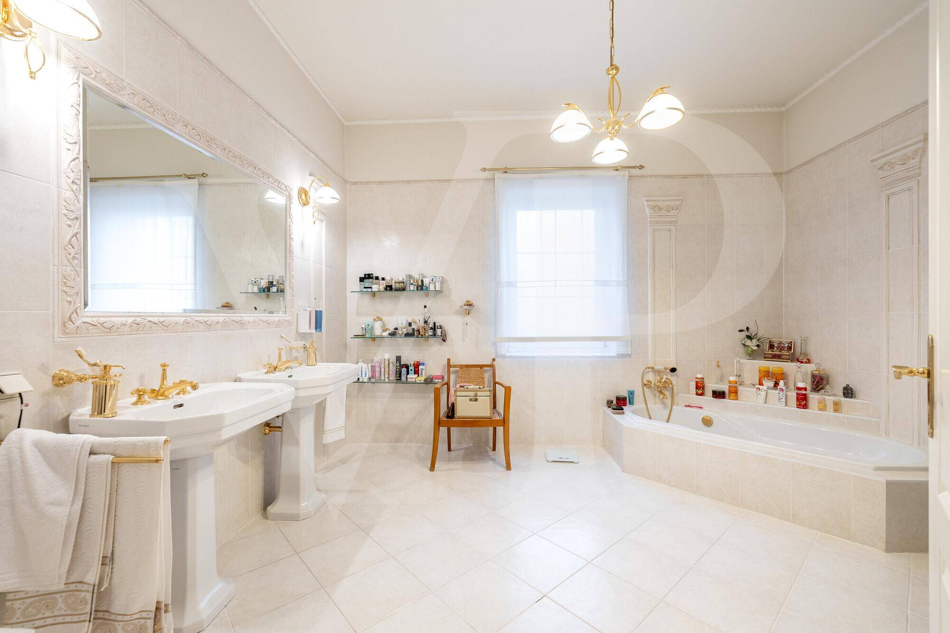 Luxuriöses Badezimmer mit Doppelwaschbecken, Badewanne und goldenen Armaturen.
