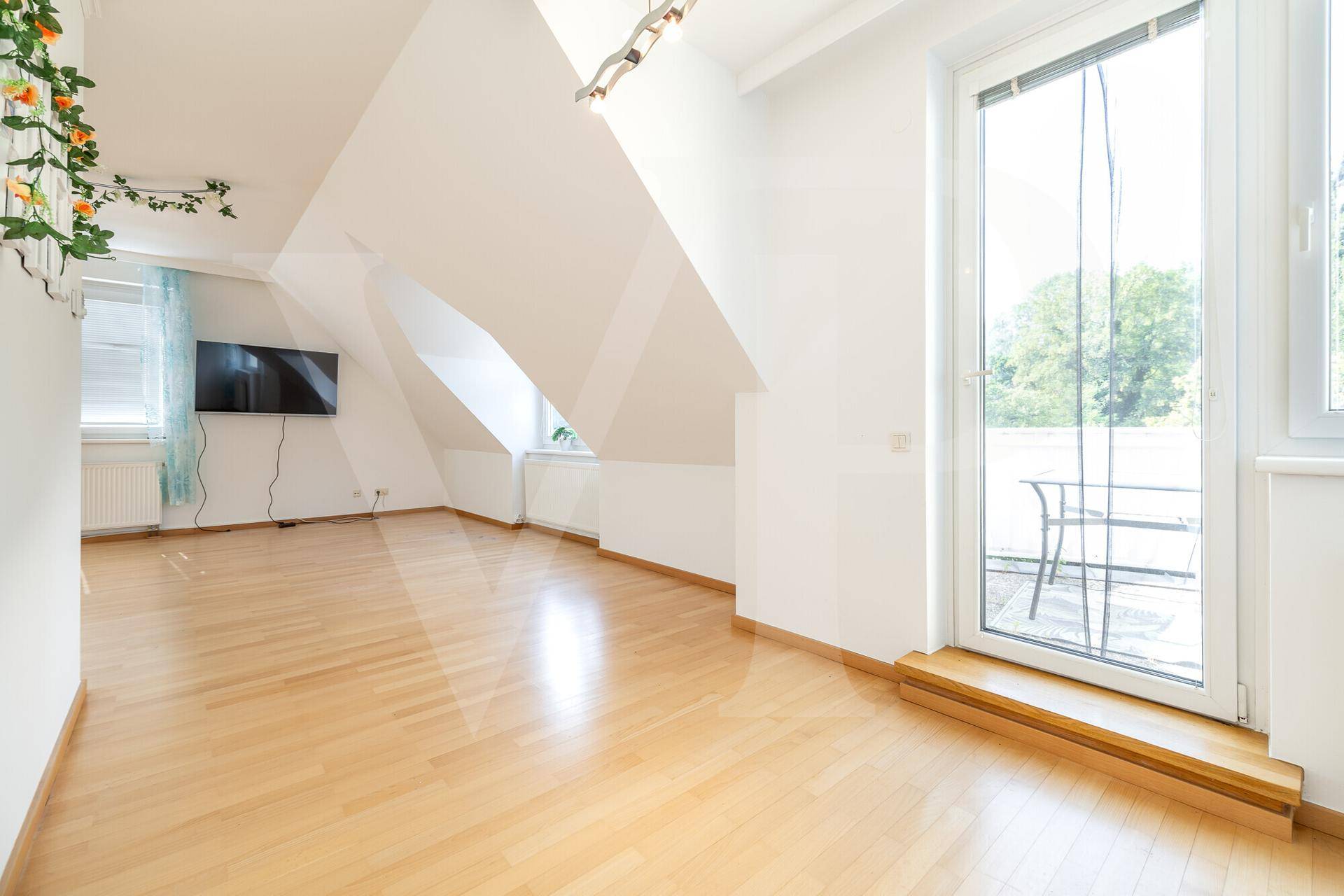Heller Raum im Dachgeschoss mit Zugang zu einem Balkon und schrägen Decken.