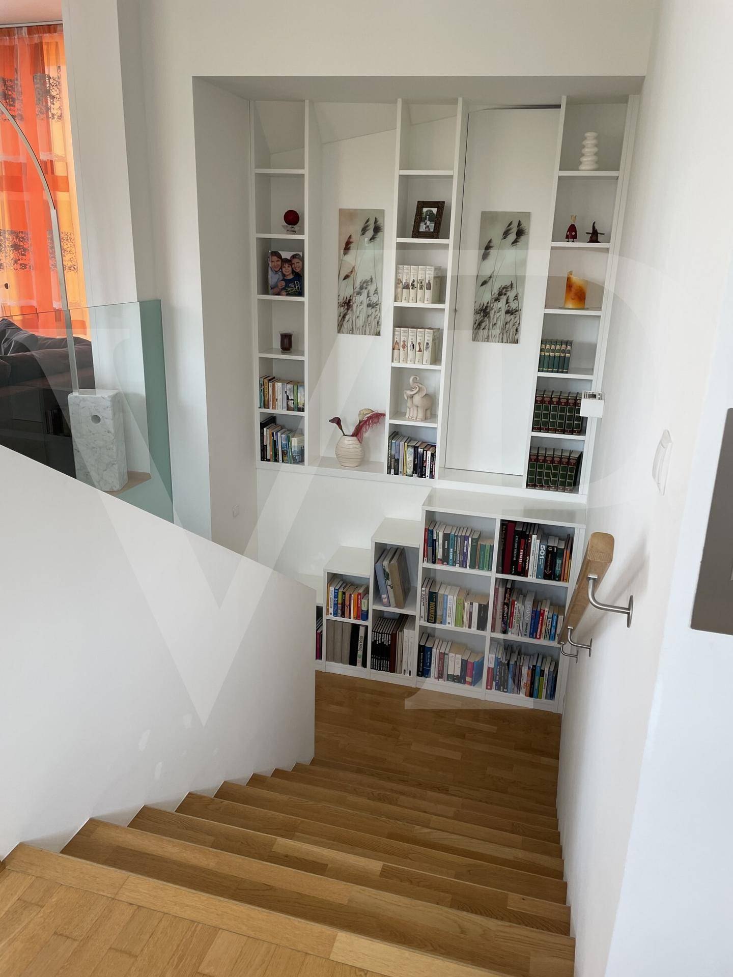Helles Treppenhaus mit Holzstufen und integrierten Bücherregalen an der Wand.