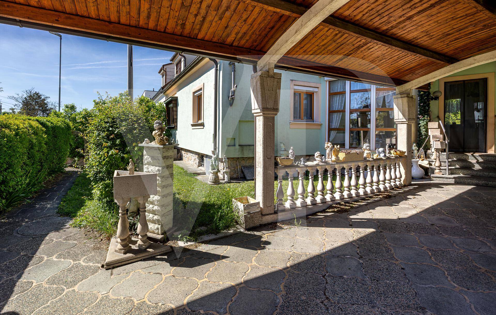 Überdachter Carport-Bereich mit gepflastertem Boden und Zugang zum Hauseingang.