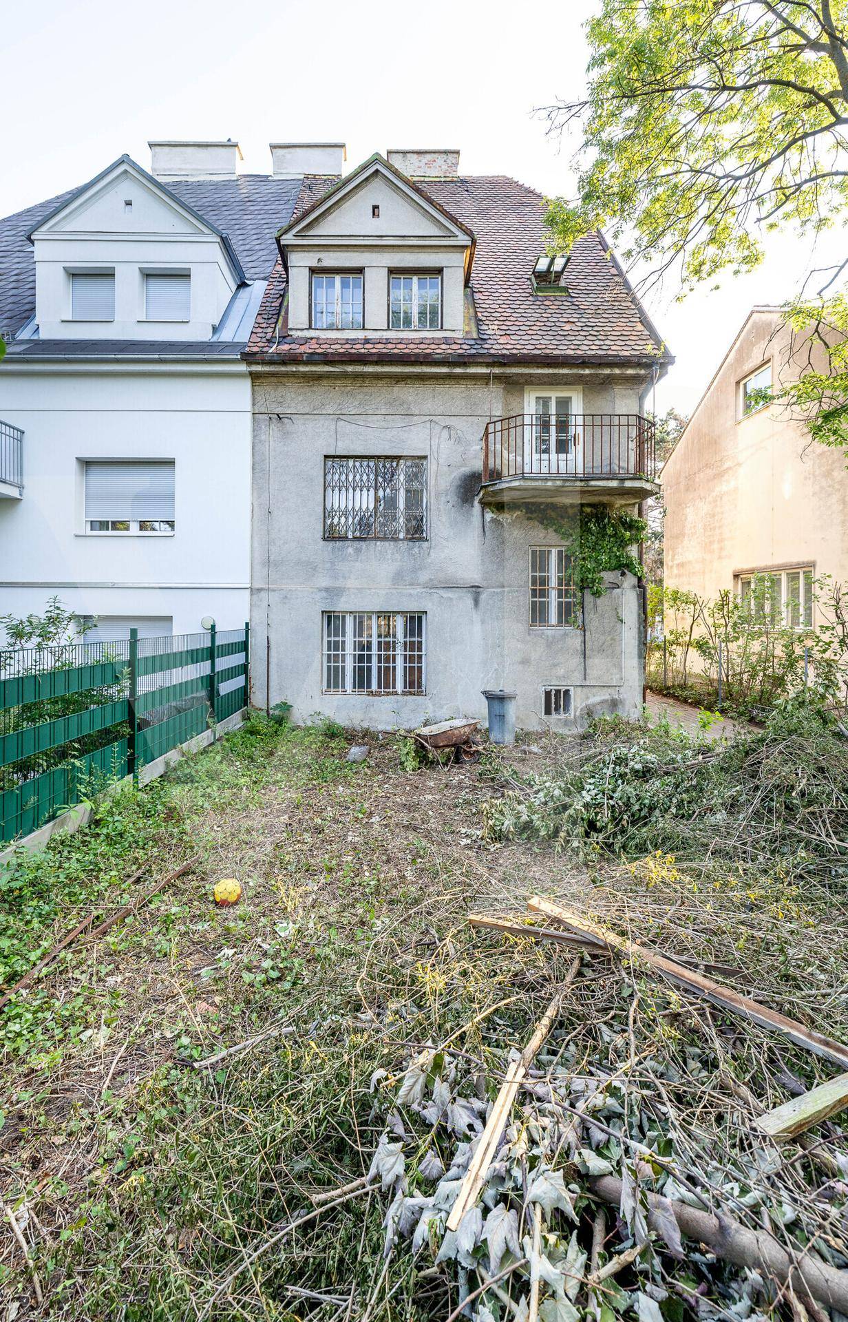 Hinterer Gartenbereich des Gebäudes in unrenoviertem Zustand mit überwuchertem Boden und Gartenabfällen.