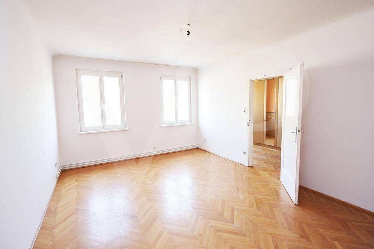 Helles, leeres Wohnzimmer mit frisch gestrichenen weißen Wänden und Fischgrätparkett.