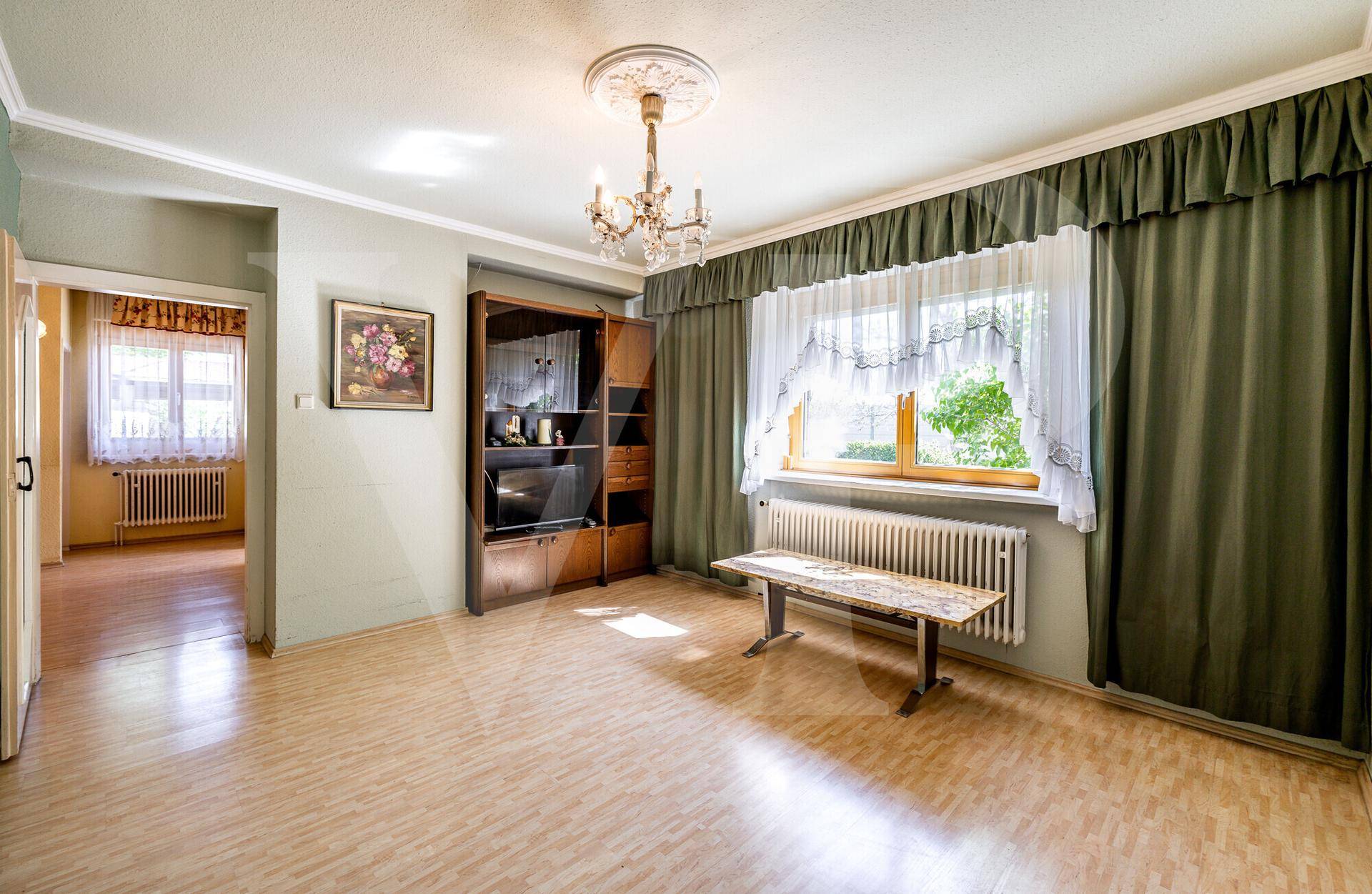 Geräumiges Wohnzimmer mit Laminatboden, grünen Wänden und einem großen Fenster.