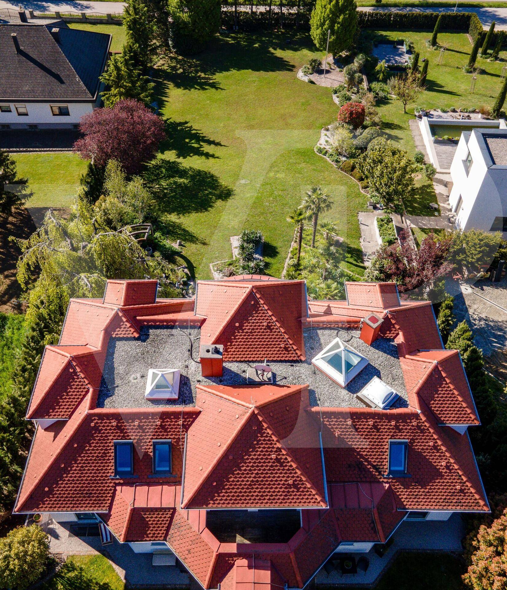 Dachansicht der Villa mit mehreren Gauben und Dachfenstern, umgeben von viel Grün und Bäumen.