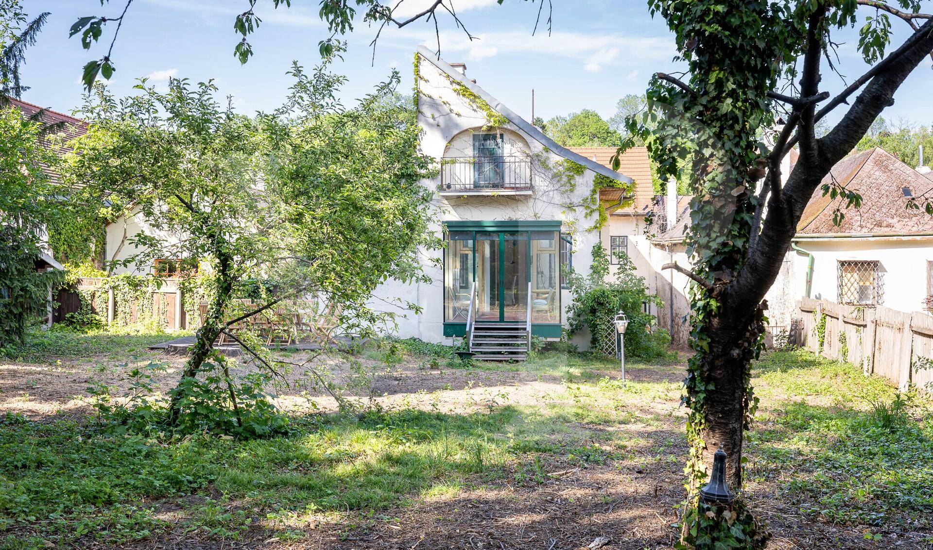 Gepflegter Garten mit Rasenfläche und einem historischen Haus mit Balkon und Wintergarten.