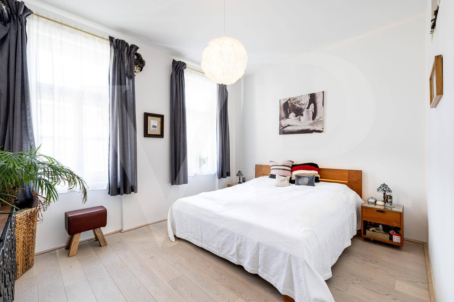 Helles Schlafzimmer mit Doppelbett, Holzboden und großen Fenstern.