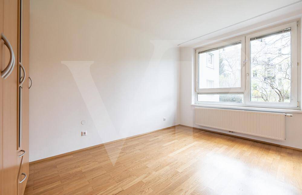 Helles Schlafzimmer mit Parkettboden, großem Fenster und Einbauschrank.
